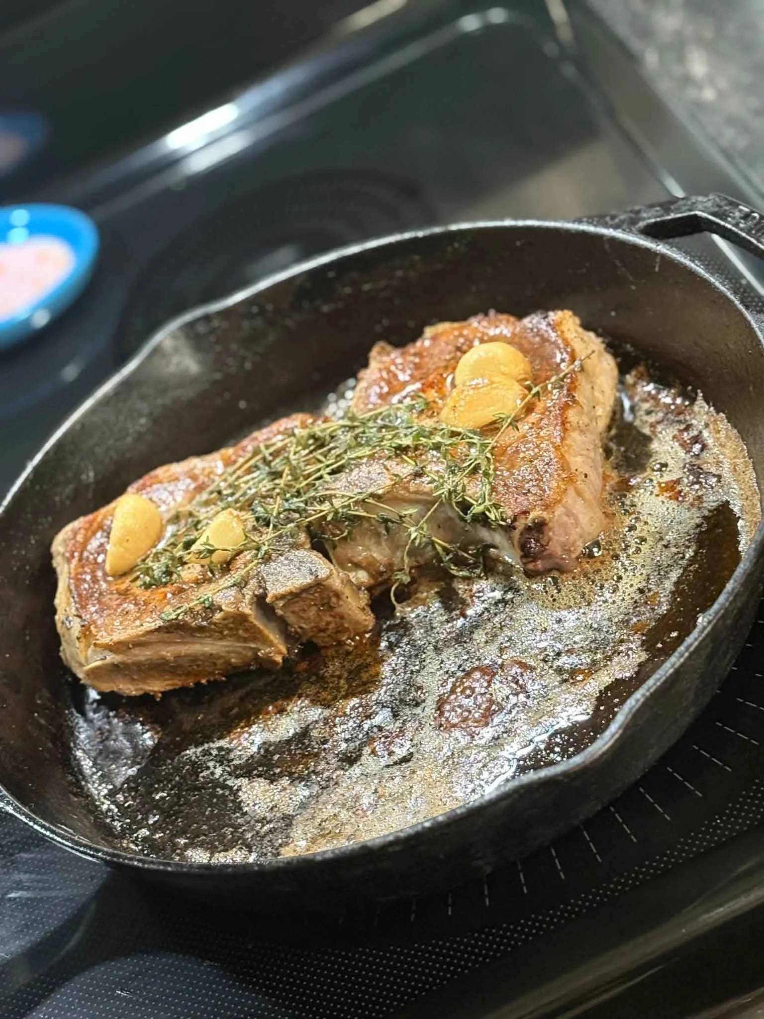 A cooked piece of meat in a cast iron skillet, garnished with garlic slices and fresh thyme, on an electric stove.