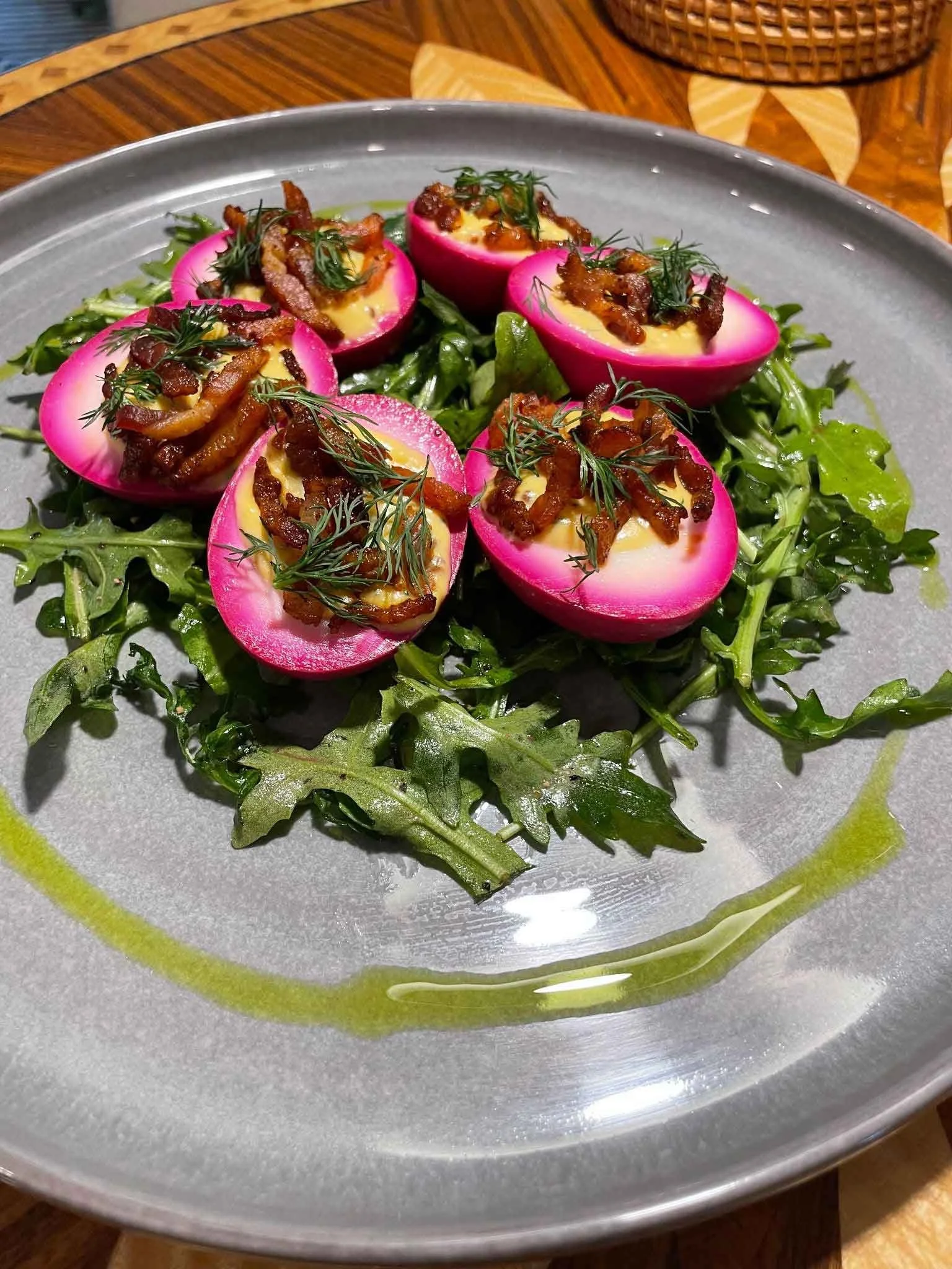 Radish halved and stuffed with creamy yellow filling, topped with crispy bacon and garnished with fresh herbs, served on a bed of leafy greens with a green sauce drizzled around the plate.