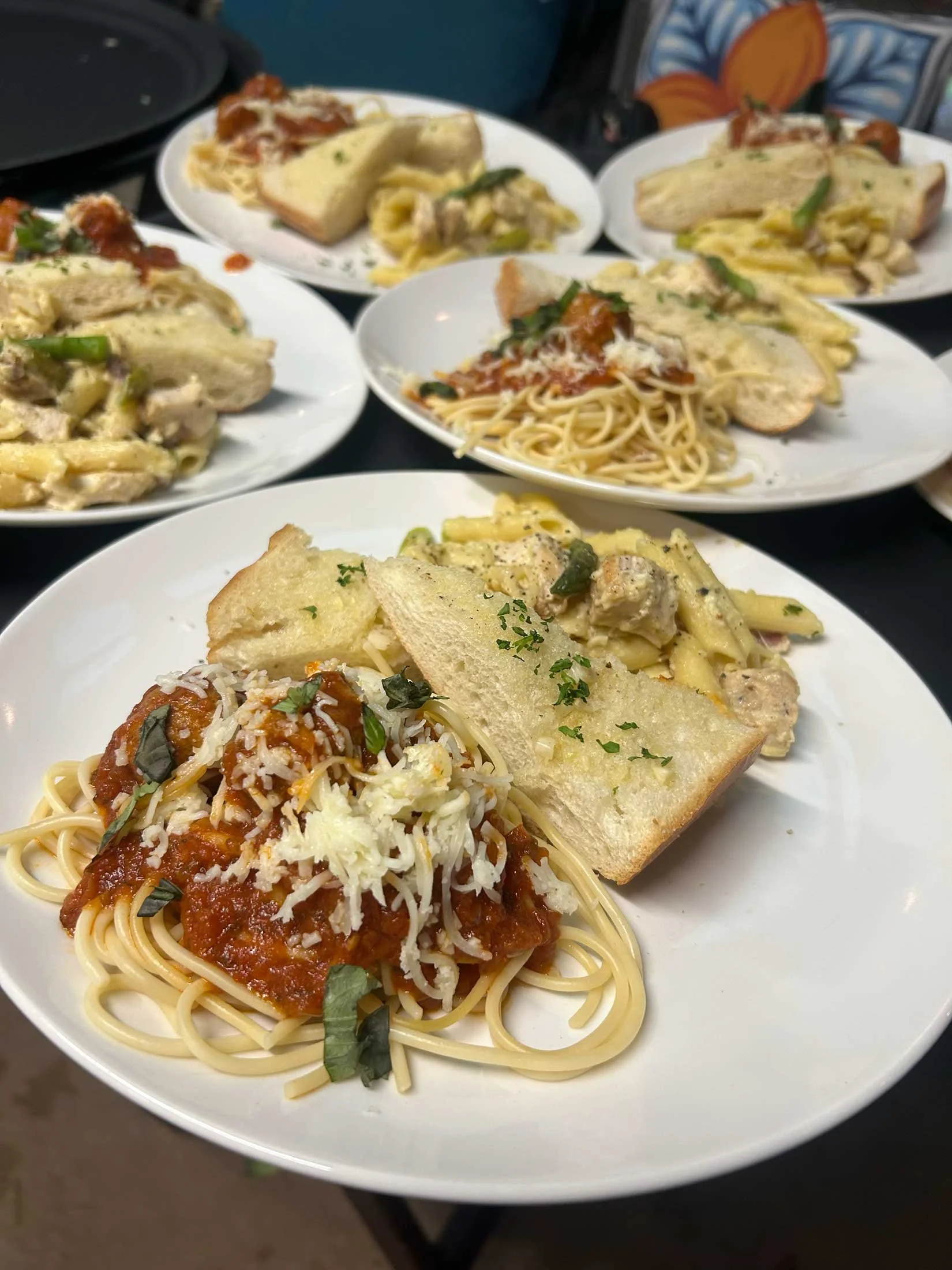 Close-up of a white plate with spaghetti topped with tomato sauce and grated cheese, accompanied by slices of garlic bread.