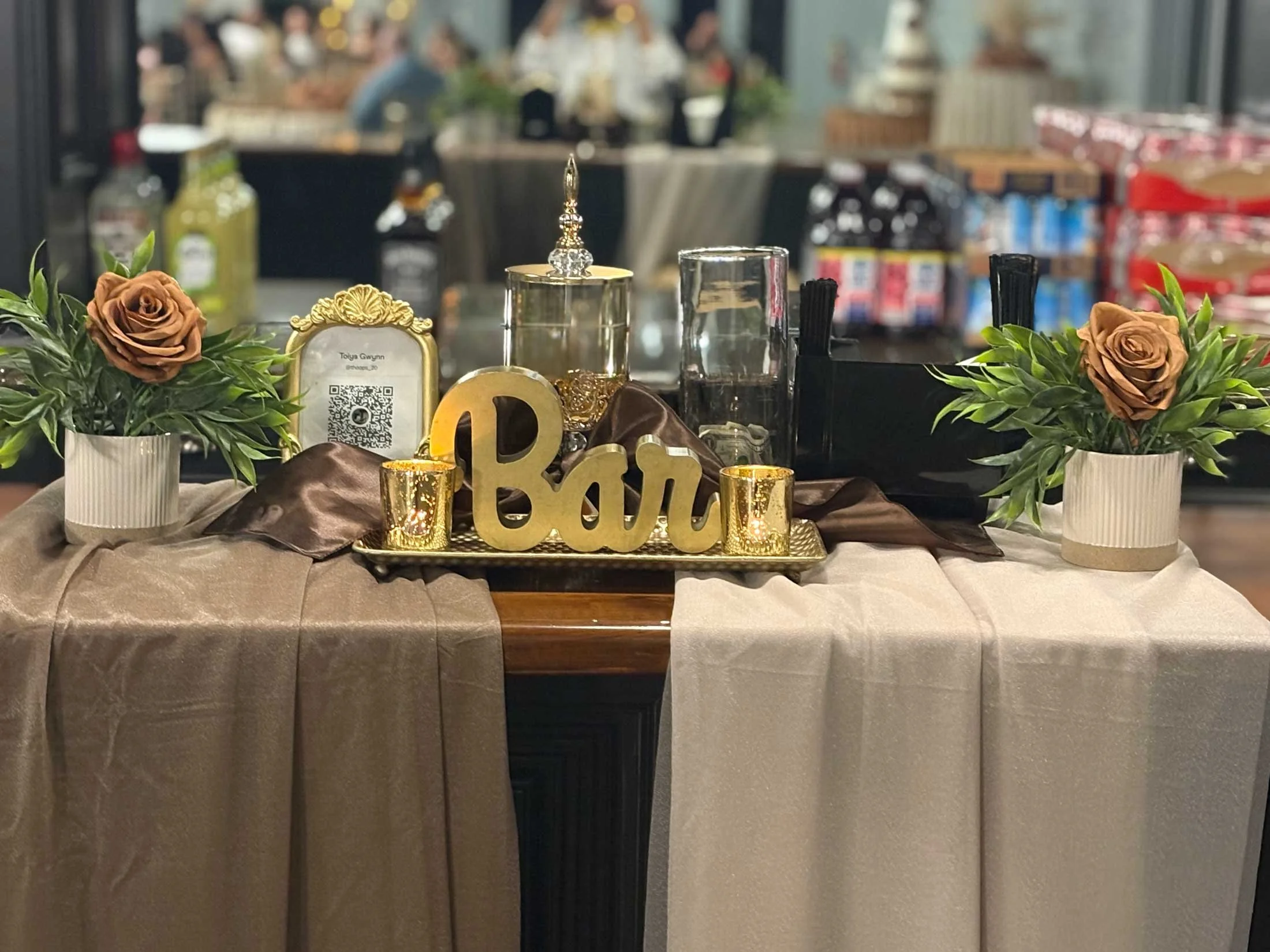 A decorated table with gold and black accents, pink roses in white vases, candles, and a 'love' sign, set against an indoor setting with blurred background.