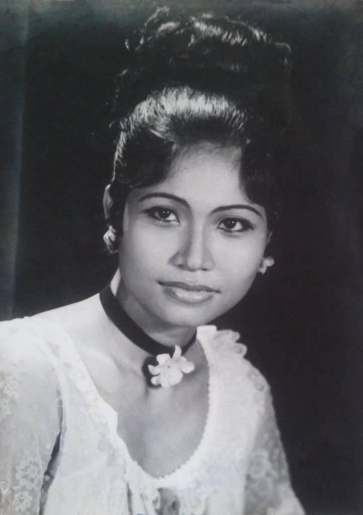 Black and white portrait of a young woman with styled hair, wearing a lace dress and a floral choker necklace.
