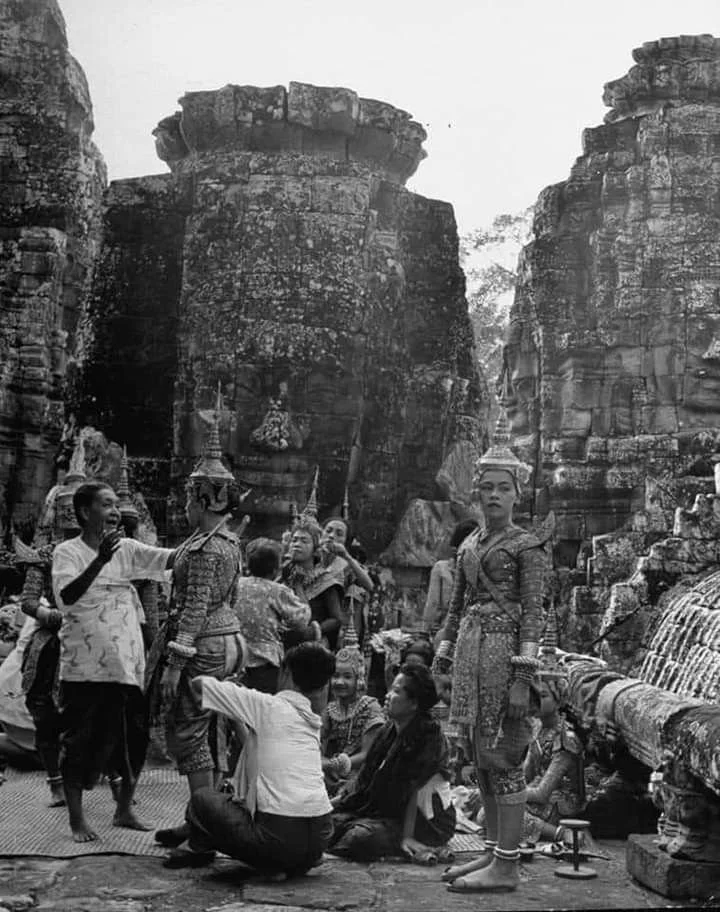People dressed in traditional Thai clothing gather at an ancient temple with large stone structures and waterfalls.