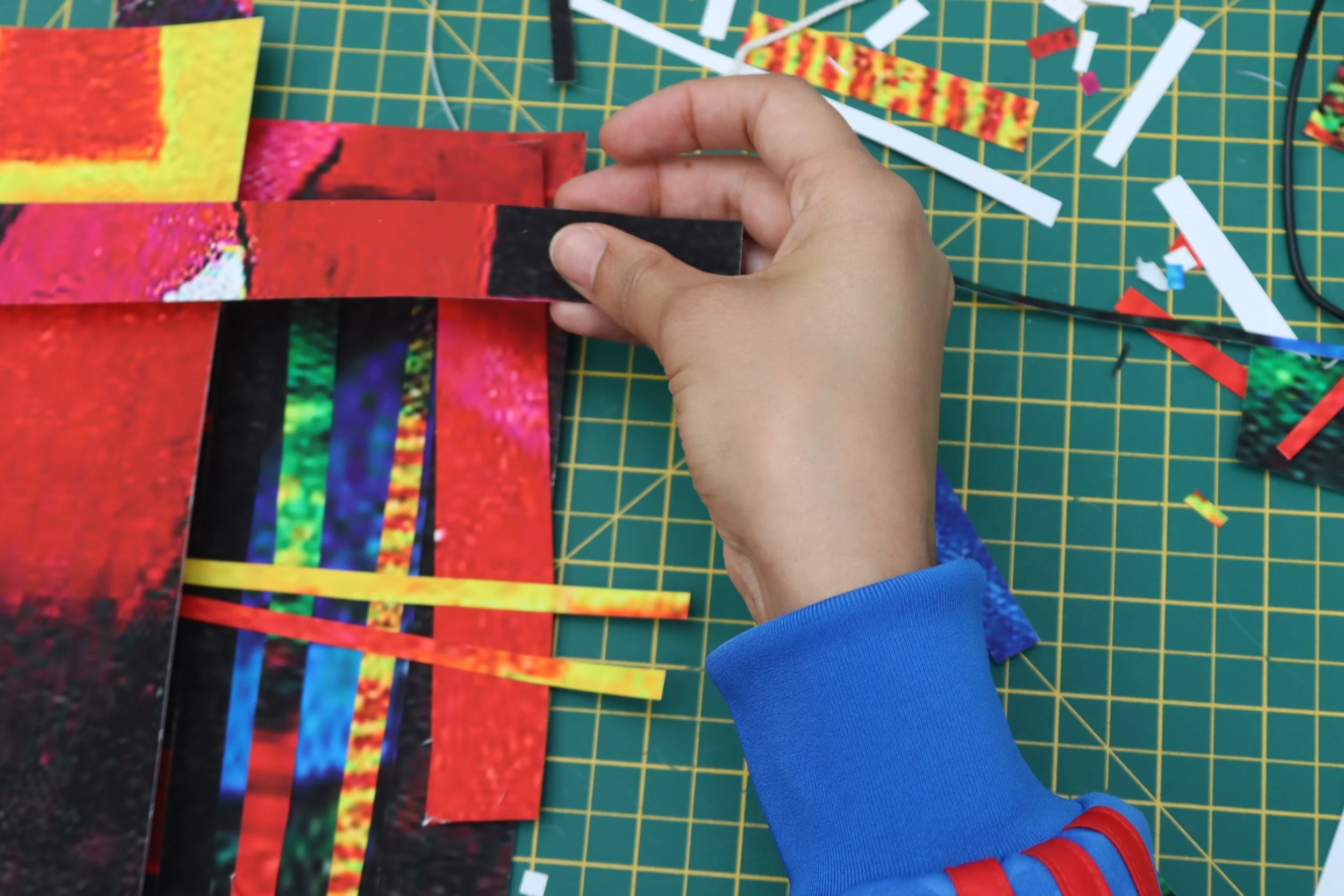 Person creating digital art collage with colourful printed strips on green cutting mat.