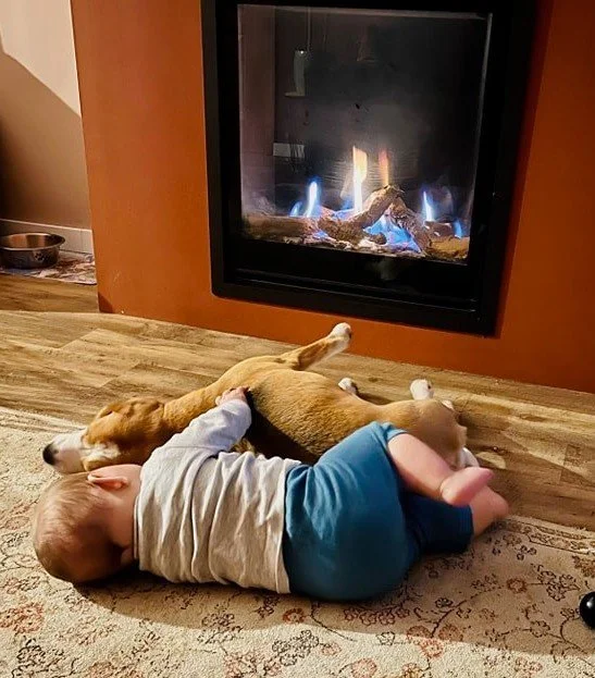 Un enfant et un chien allongés côte à côte sur un tapis devant une cheminée à feu.
