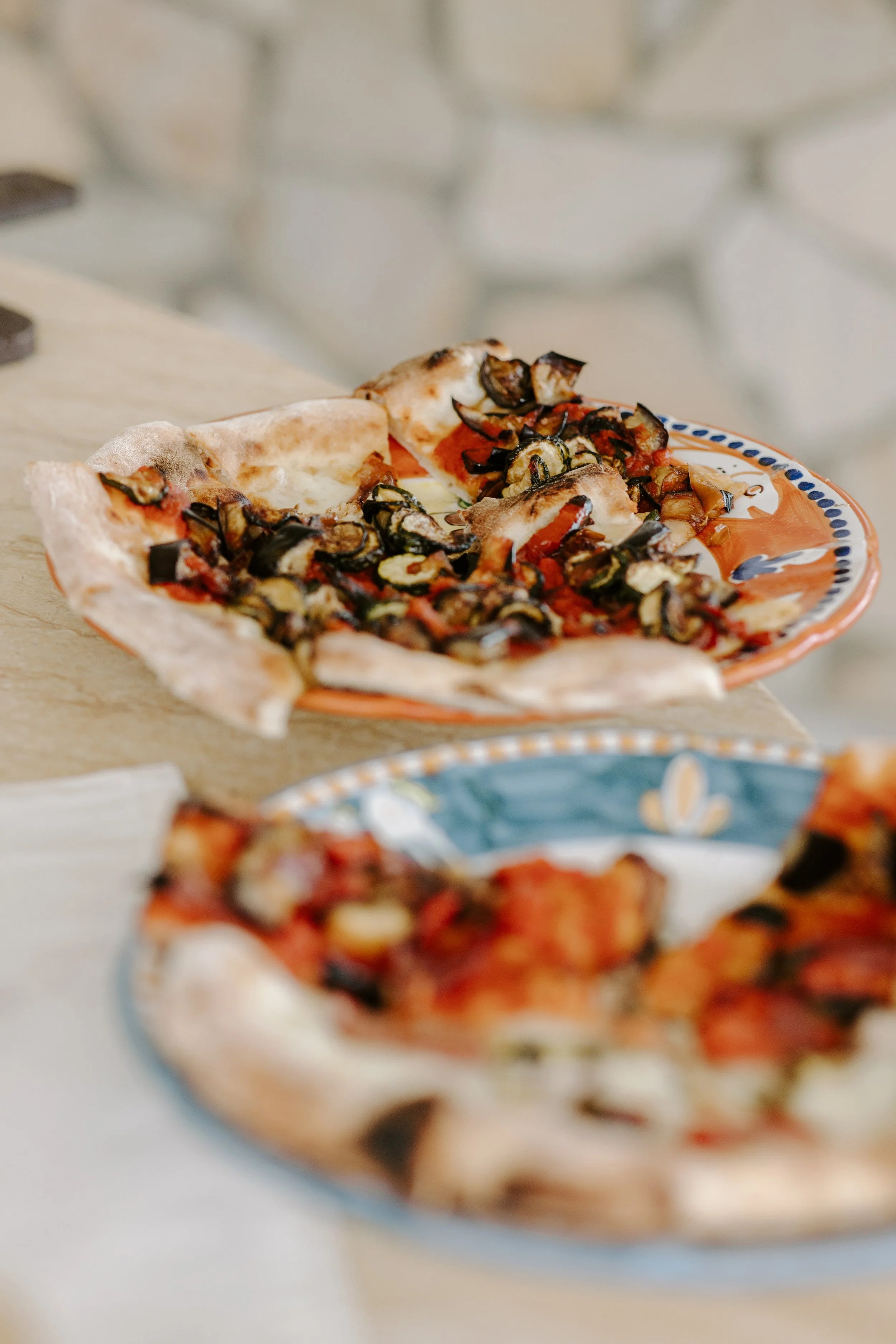 Close-up of a partially eaten small pizza with a thin crust, topped with eggplant, tomato sauce, and cheese, served on a decorative plate.