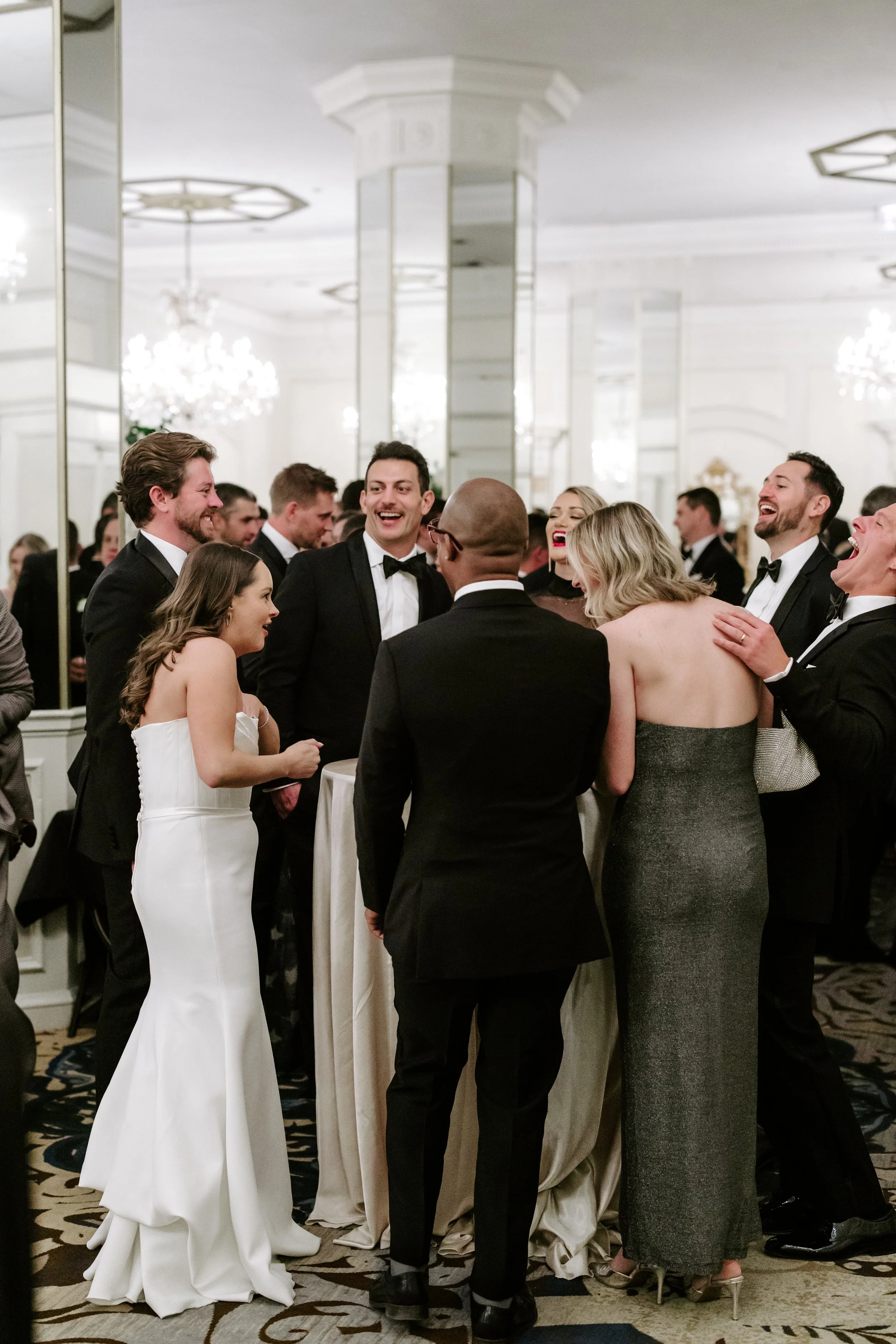 People dressed in formal attire gathered around a table at an elegant indoor event, smiling and engaging in conversation.
