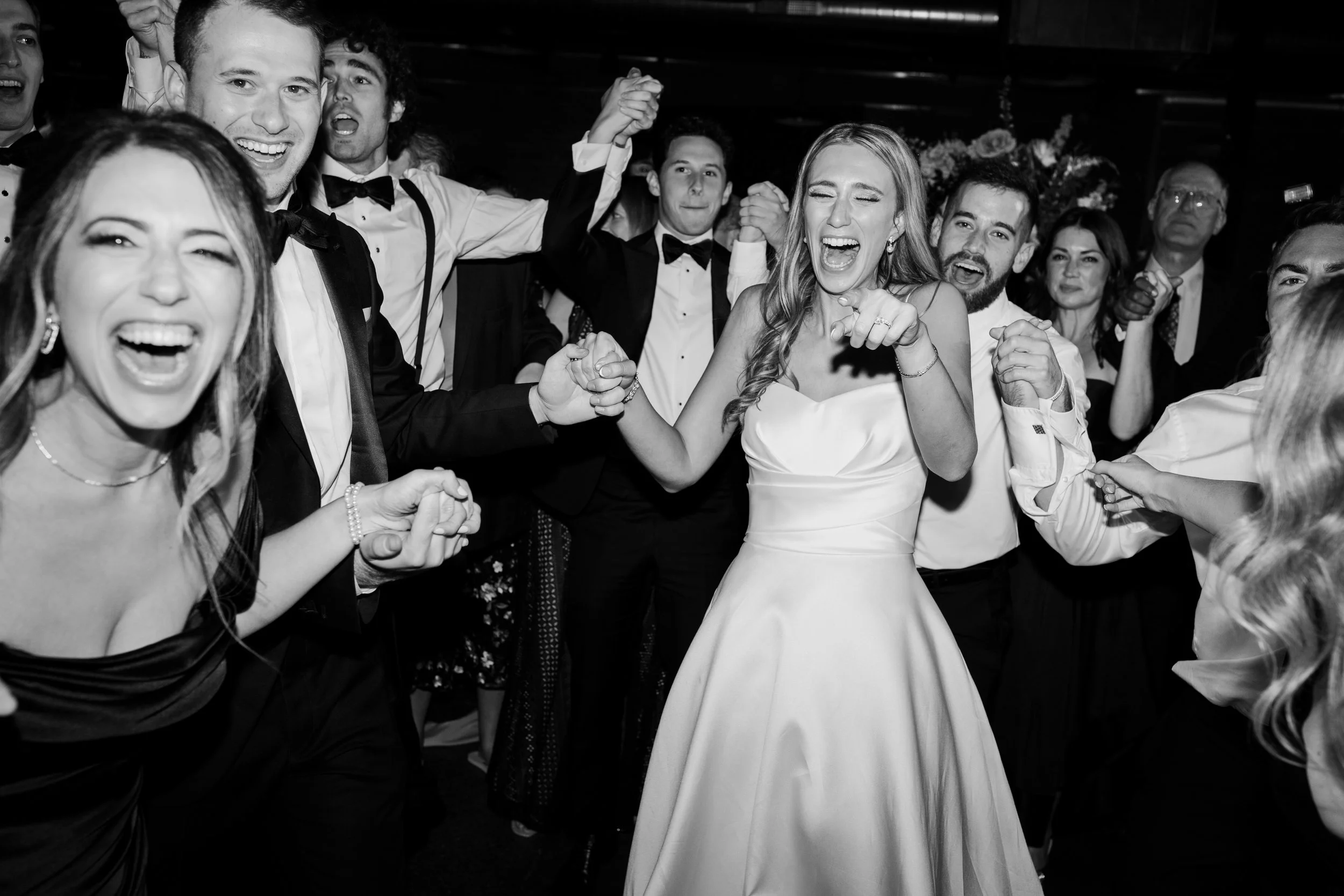 Group of people smiling, dancing, and enjoying a celebration, with a woman in a white dress in the center.