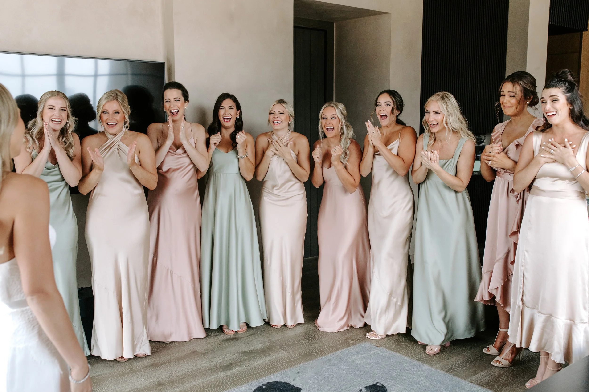 Group of women in bridesmaid dresses laughing and smiling in a modern indoor setting.