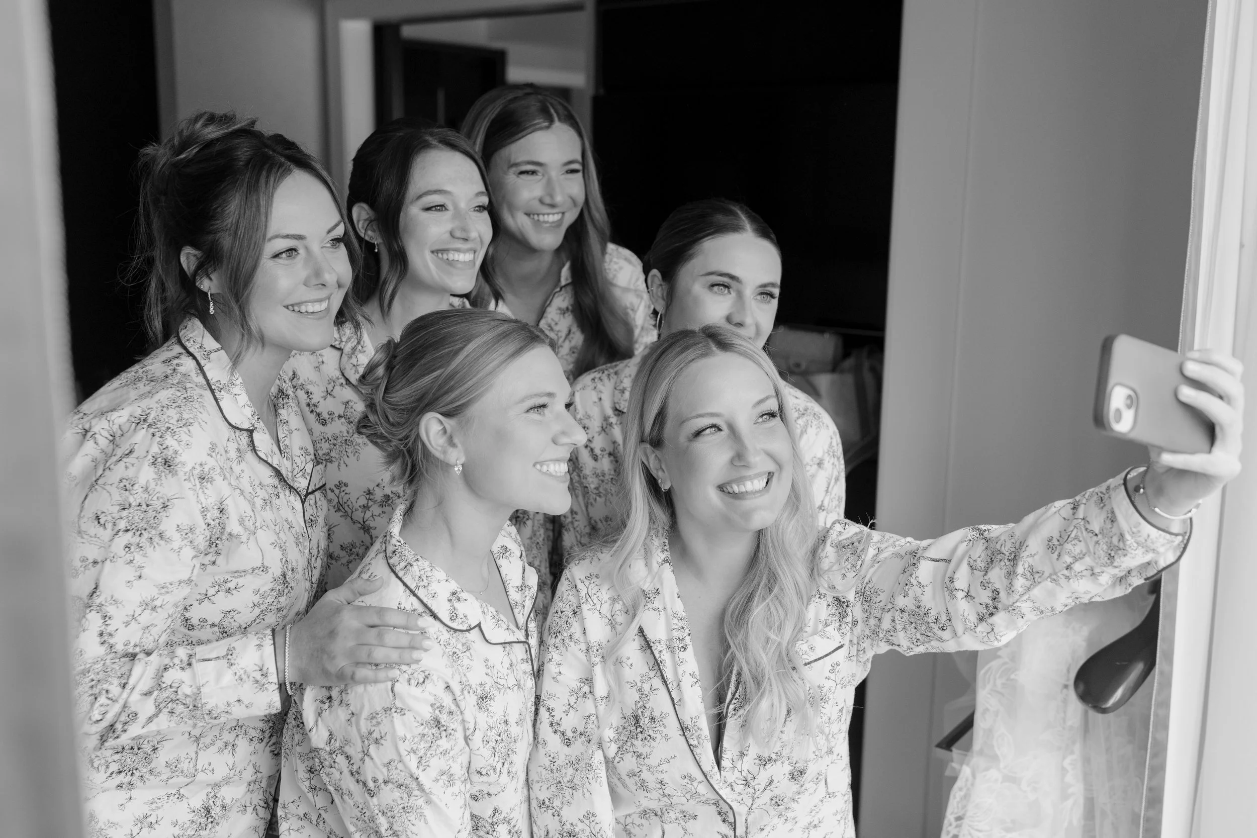 Group of six women in matching pajamas taking a selfie in front of a mirror.