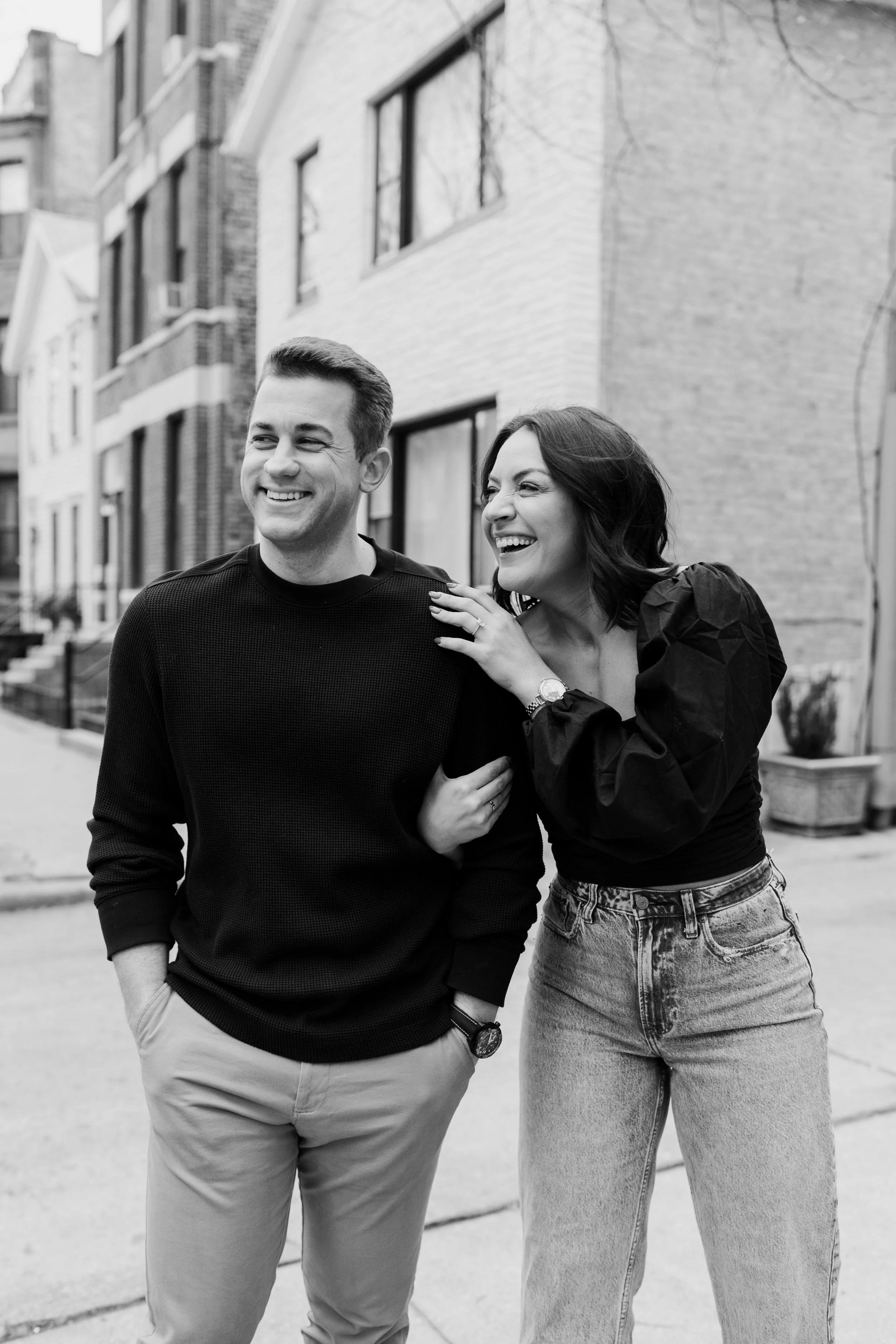 A black and white photo of a young man and woman standing on a city sidewalk, laughing and enjoying each other's company.