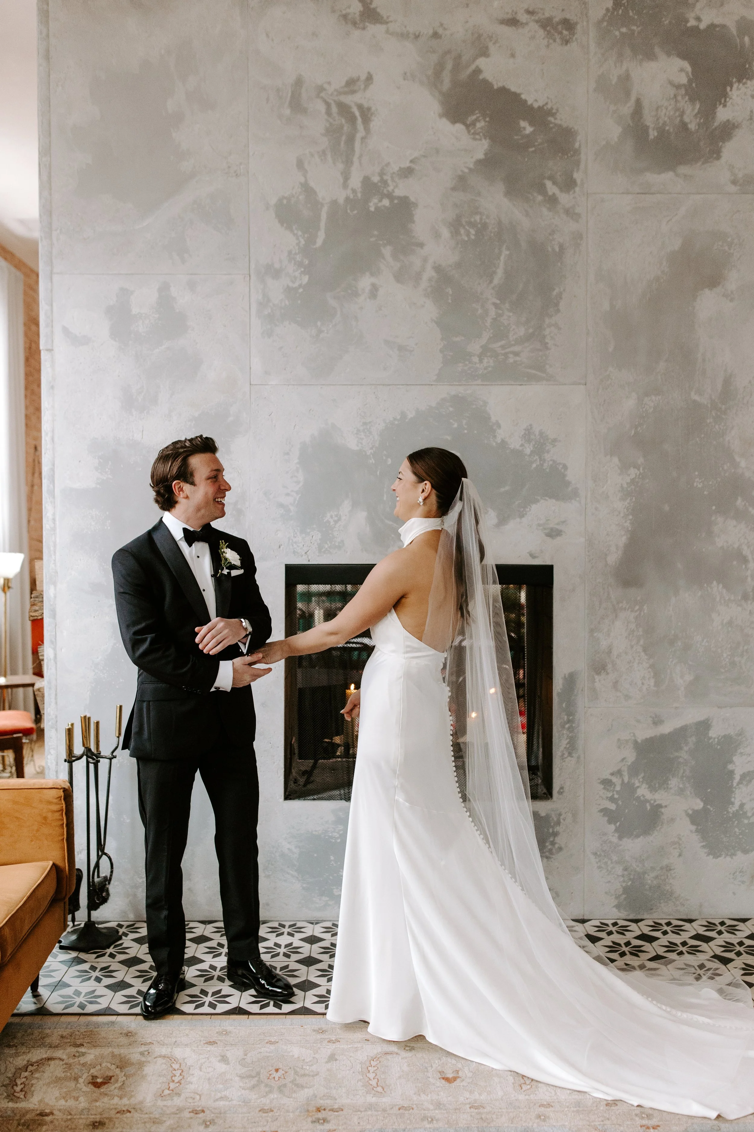 Bride and groom holding hands in front of a modern fireplace during their wedding ceremony.