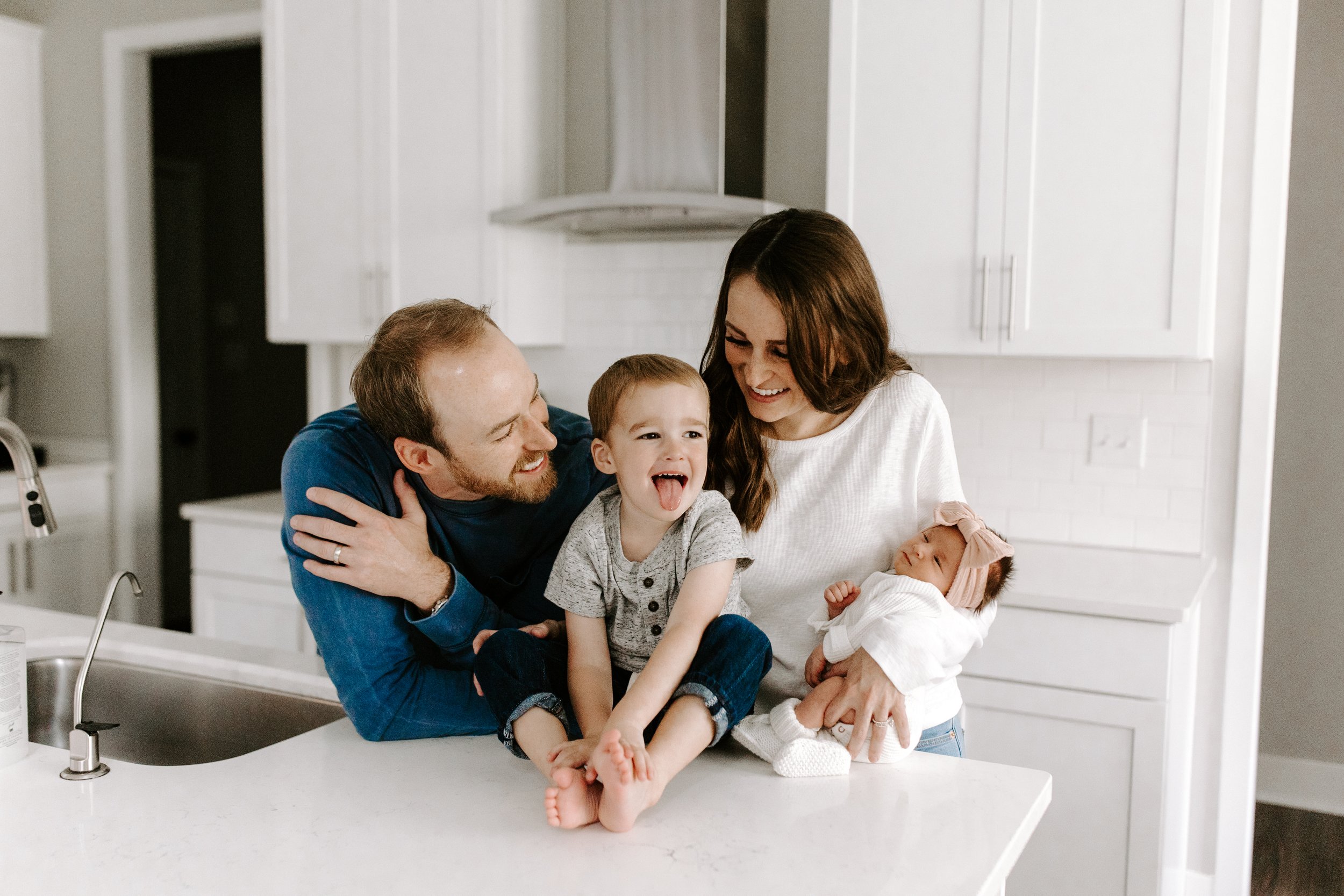 Family of five in a kitchen, smiling and laughing, with two children and a newborn baby.