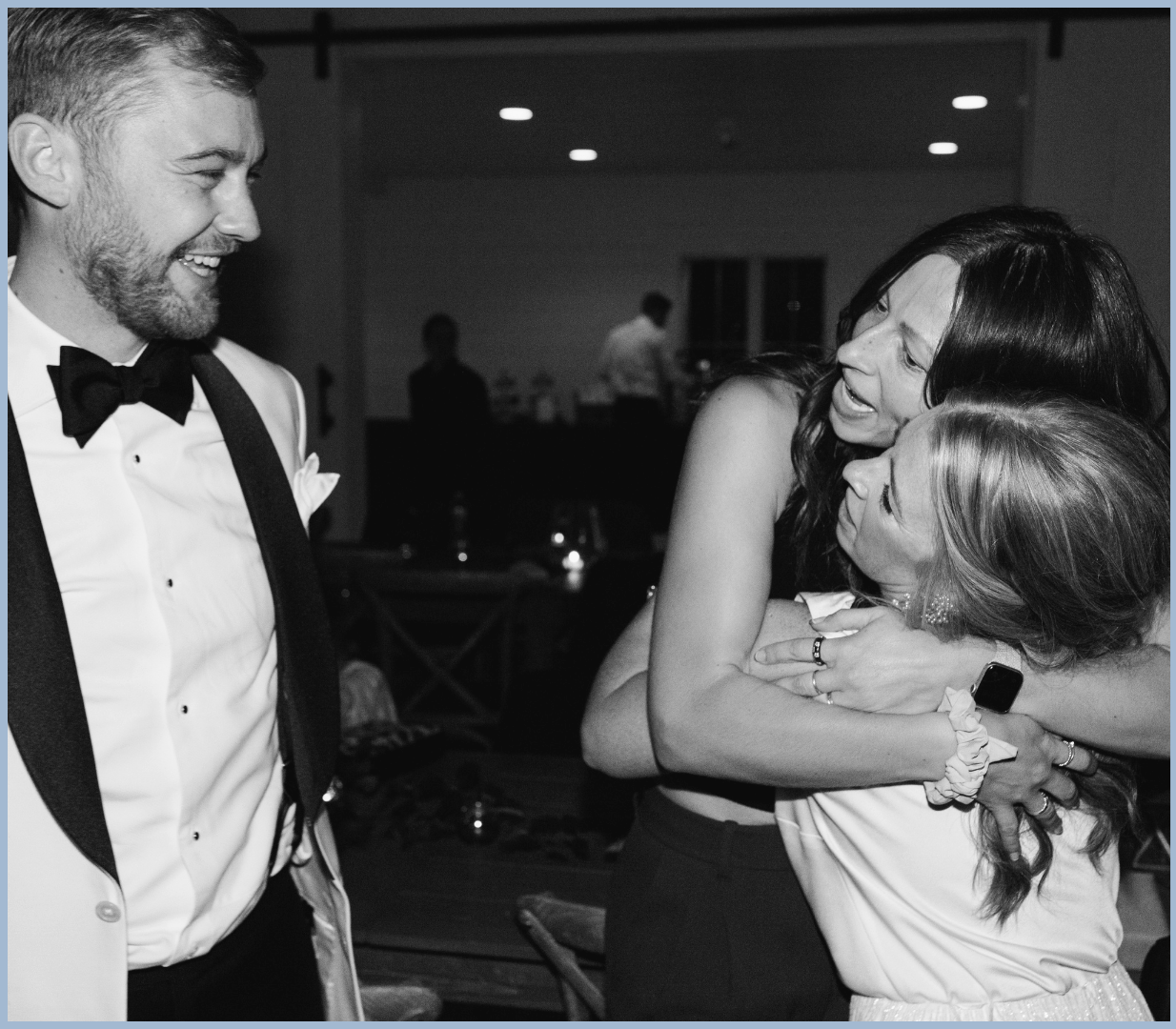 People dressed in formal attire at a celebration, sharing hugs and smiling.
