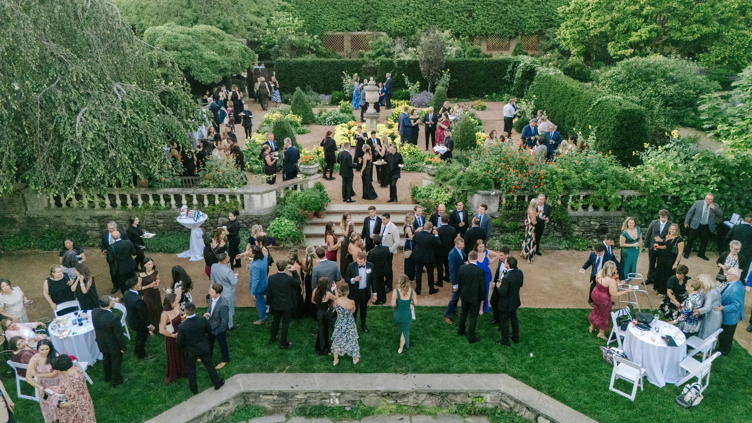 People attending an outdoor garden wedding reception with tables, chairs, and lush green landscaping.