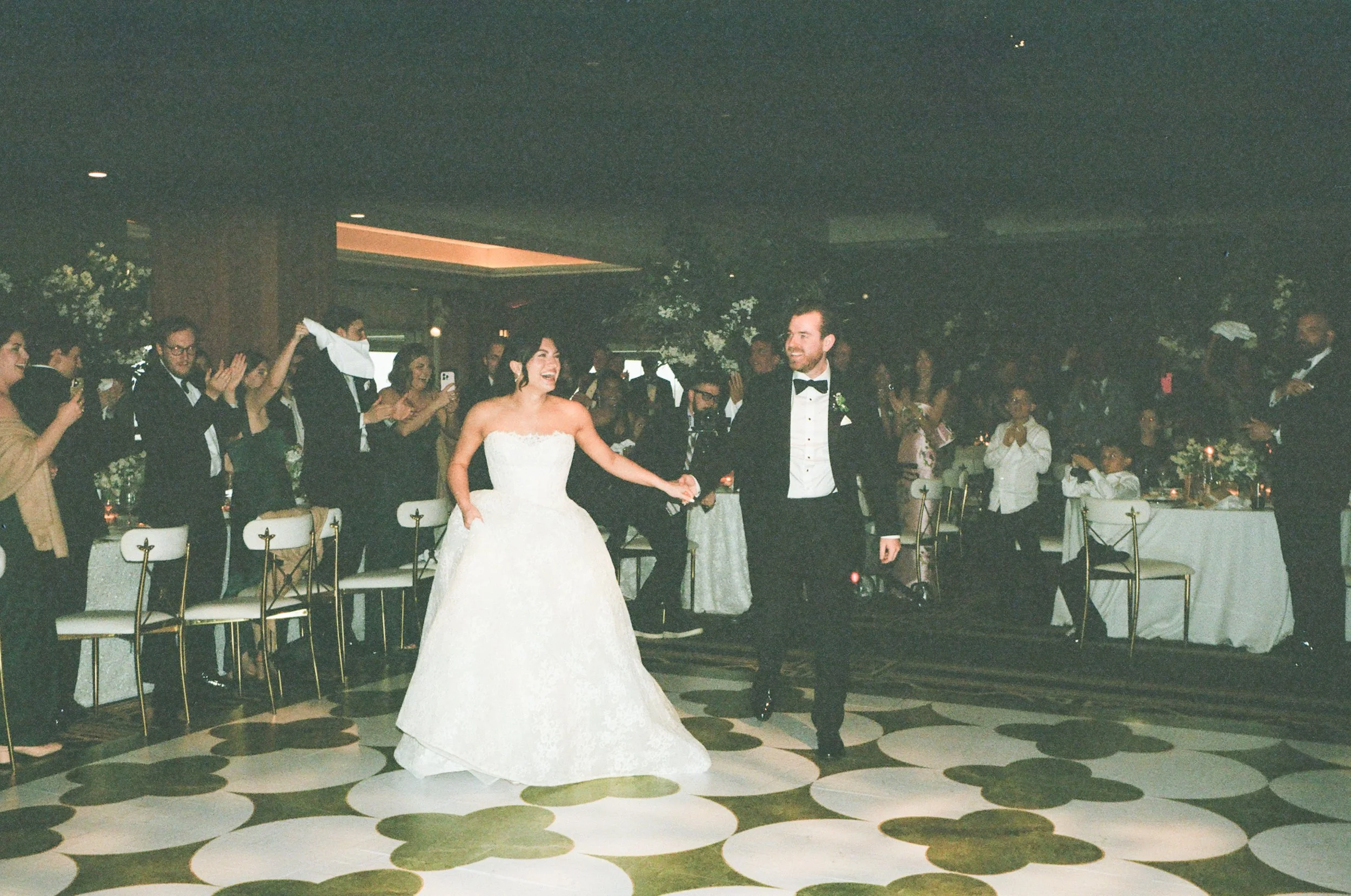 Bride and groom dancing at their wedding reception, surrounded by guests who are clapping and smiling.