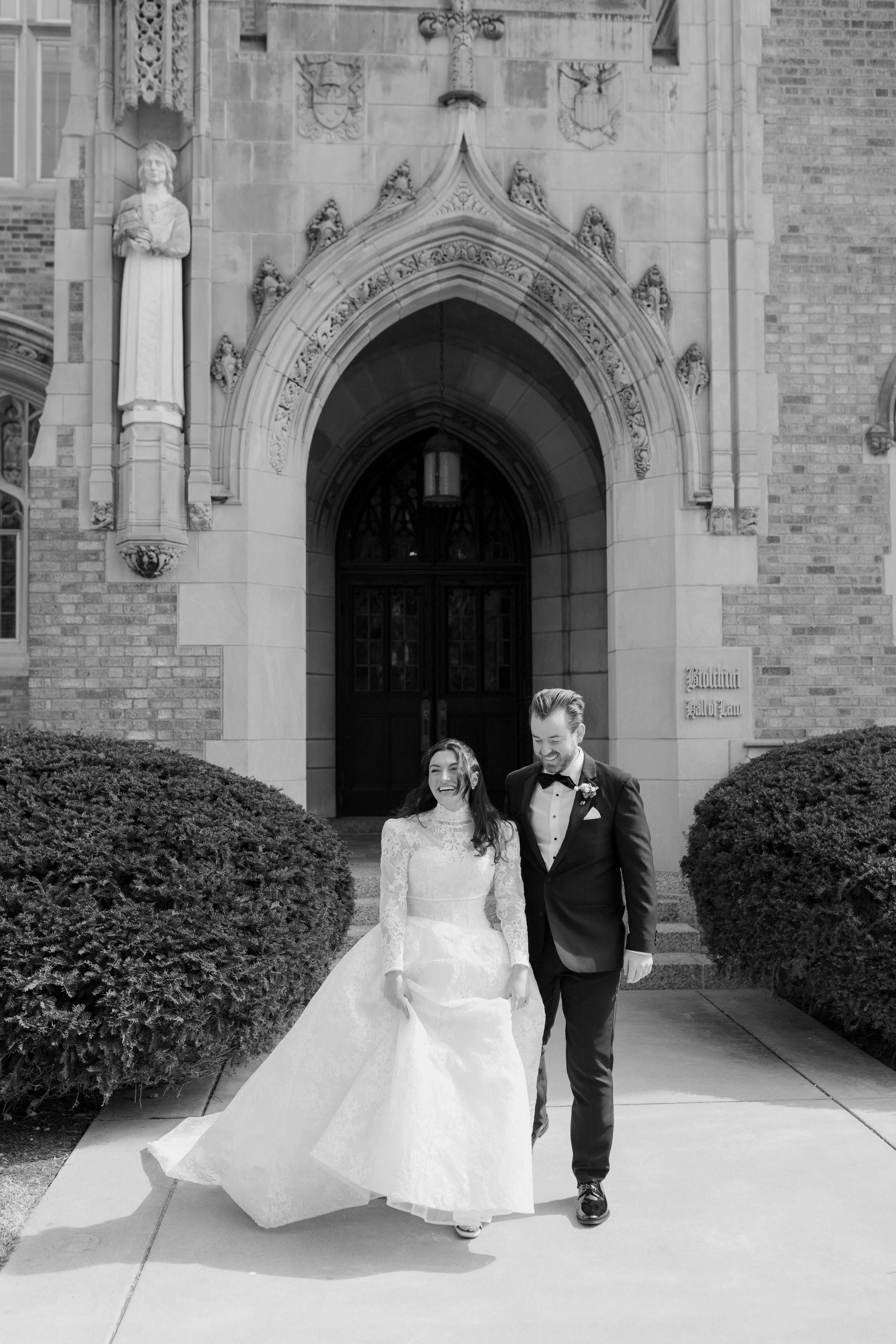 A newly married couple walking out of a church, the bride in a wedding gown and the groom in a tuxedo, smiling and holding hands.