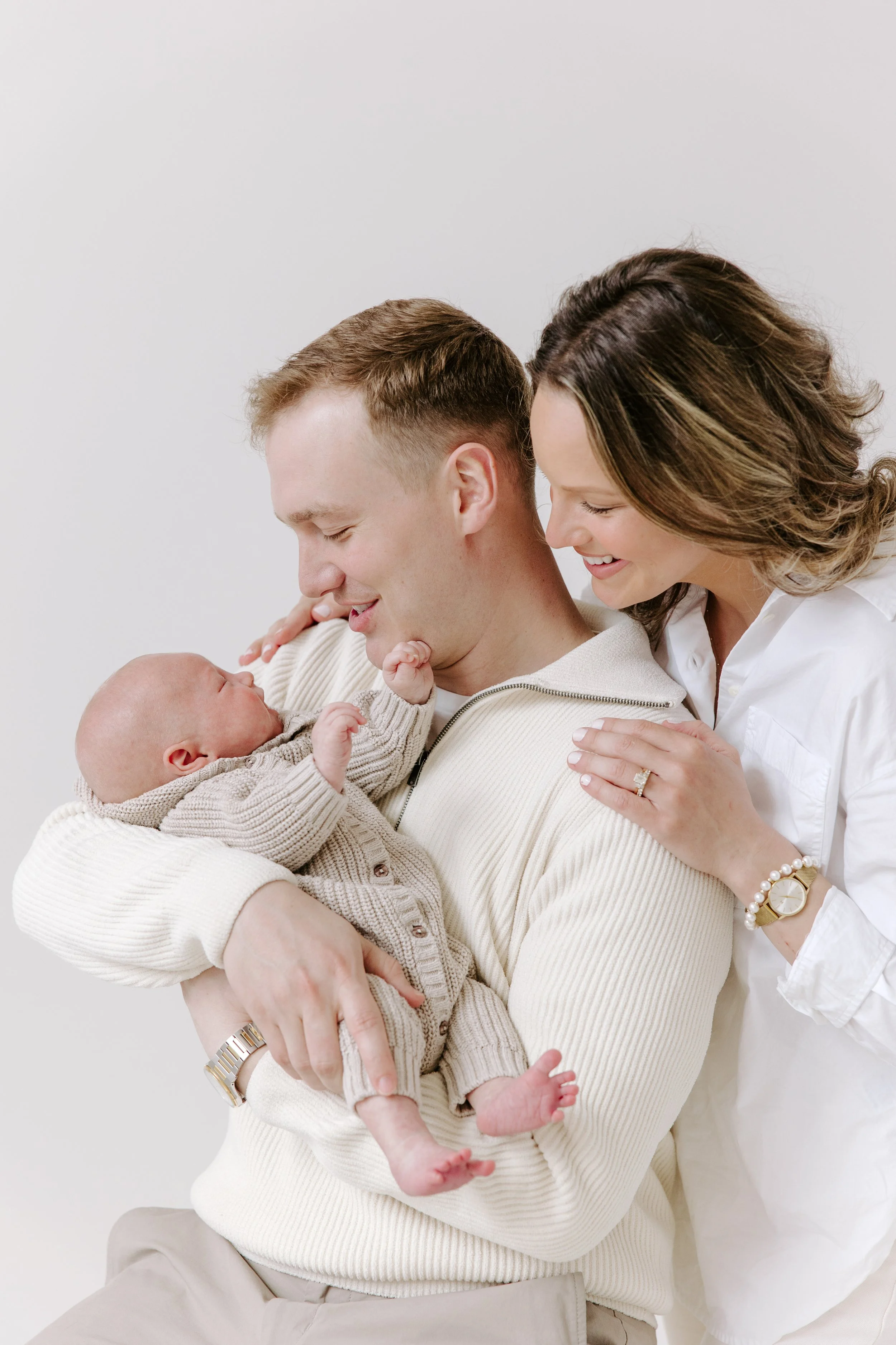 A family of three holding a newborn baby, with the father cradling the baby and the mother leaning in close, smiling.