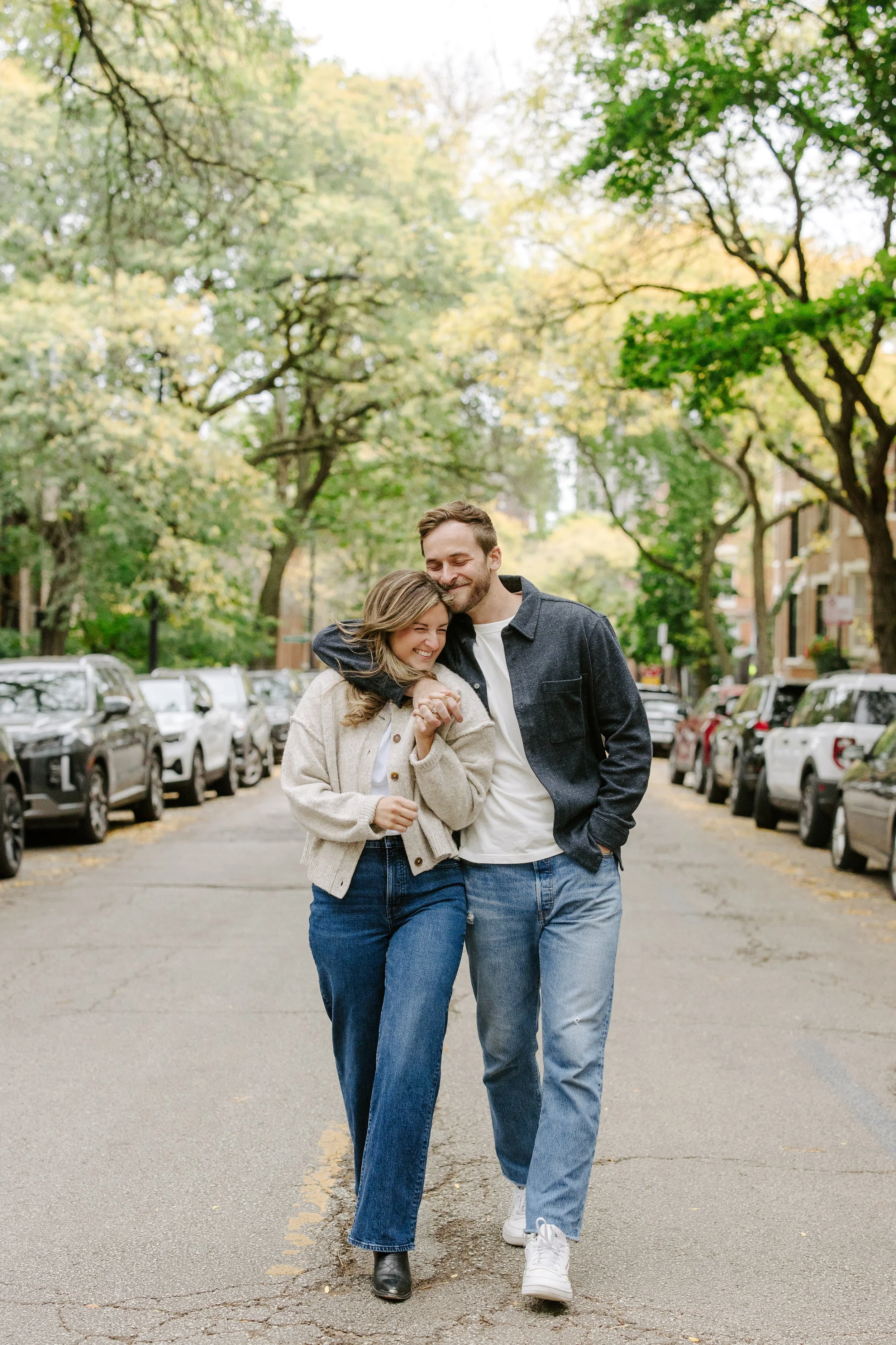 A young couple, woman and man, walking together in a park on a city street, smiling and enjoying each other's company on a fall day.