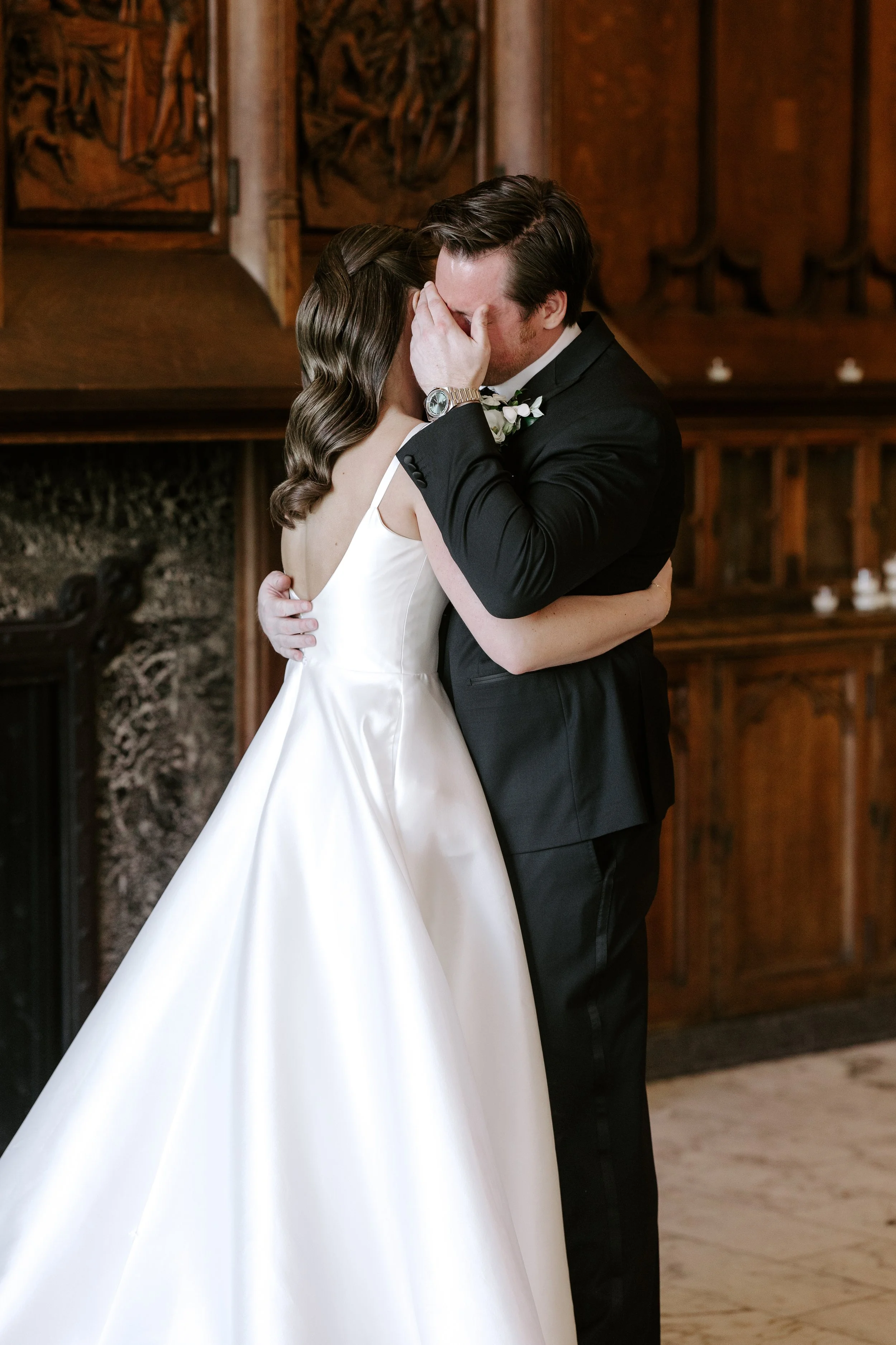 A bride and groom share a tender moment during their wedding, with the groom holding the bride's face as they prepare to kiss in an ornate wooden room.