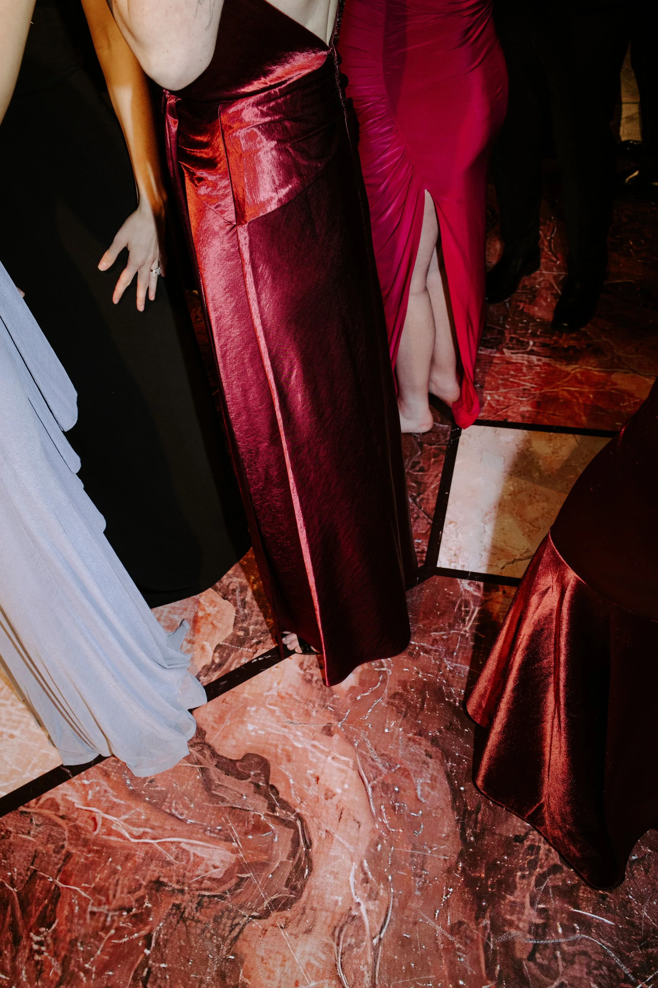 People dressed in formal evening gowns and tuxedos at a social event or party, standing on a marble floor.