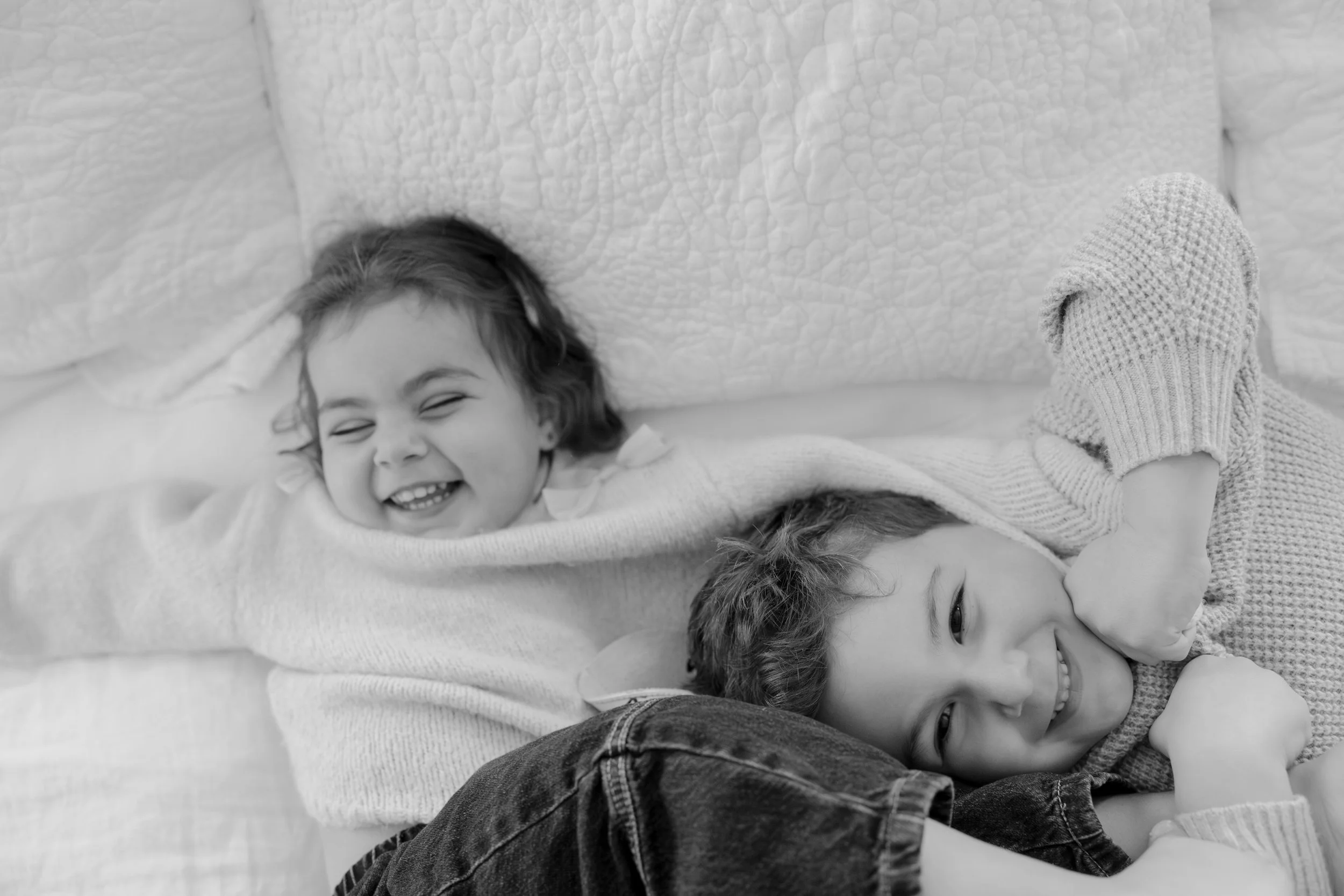 A group of children lying on a bed, smiling and laughing, with their heads close together.