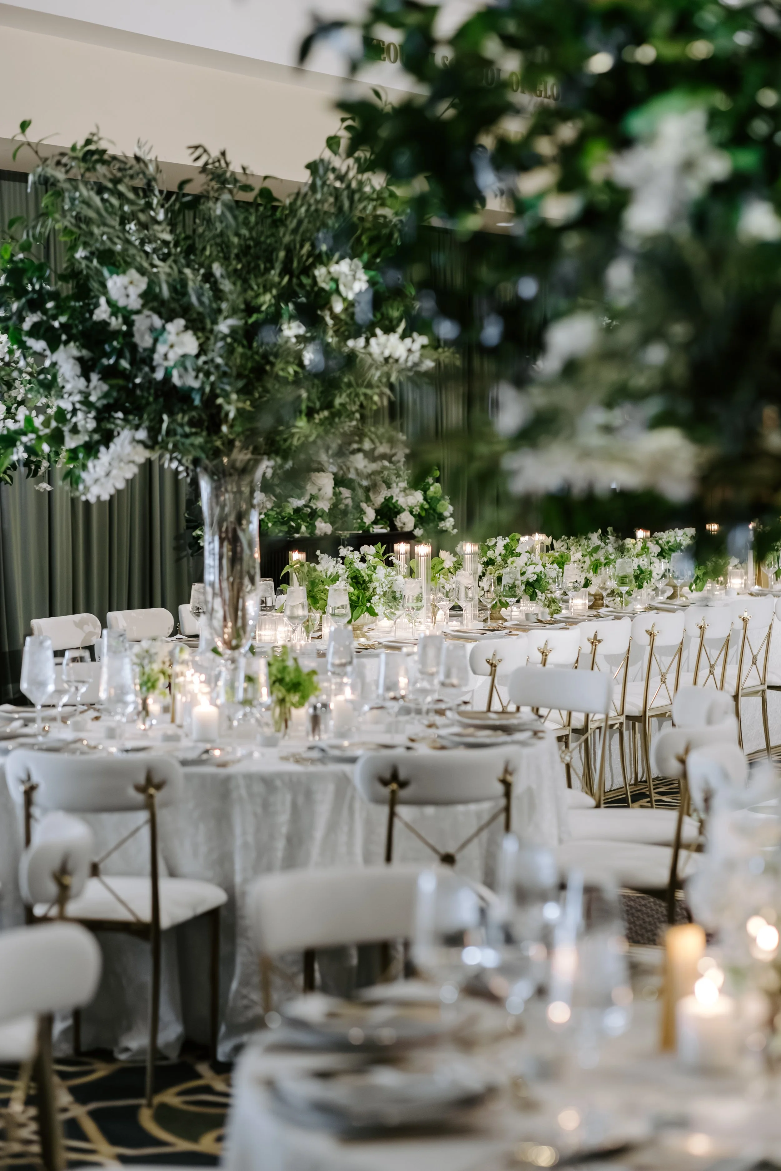 Elegant banquet hall decorated with large floral arrangements and white table settings for a formal event or wedding reception.