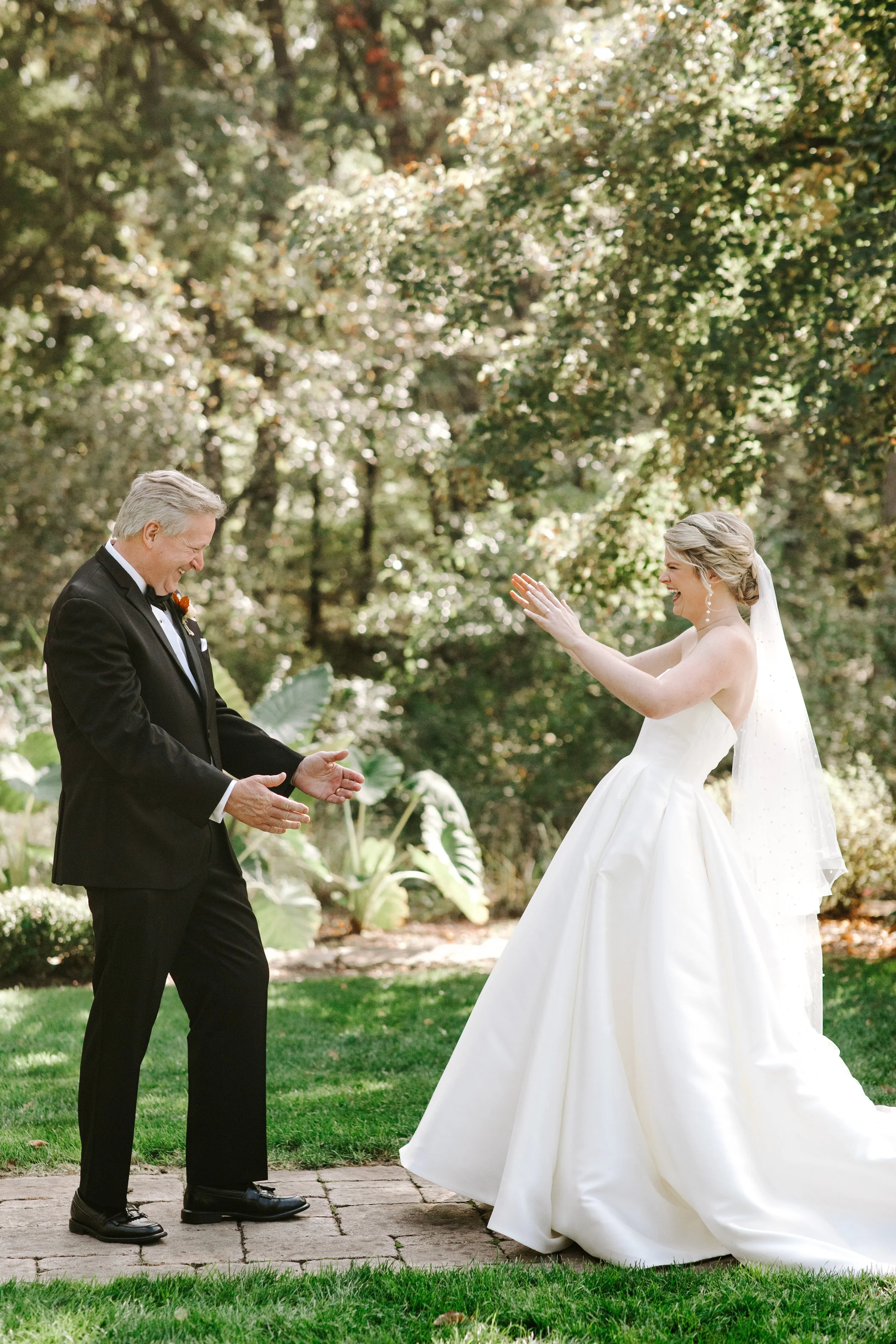 A bride and groom are celebrating outdoors, with the groom in a tuxedo and the bride in a white wedding gown, both smiling and laughing in a garden setting.