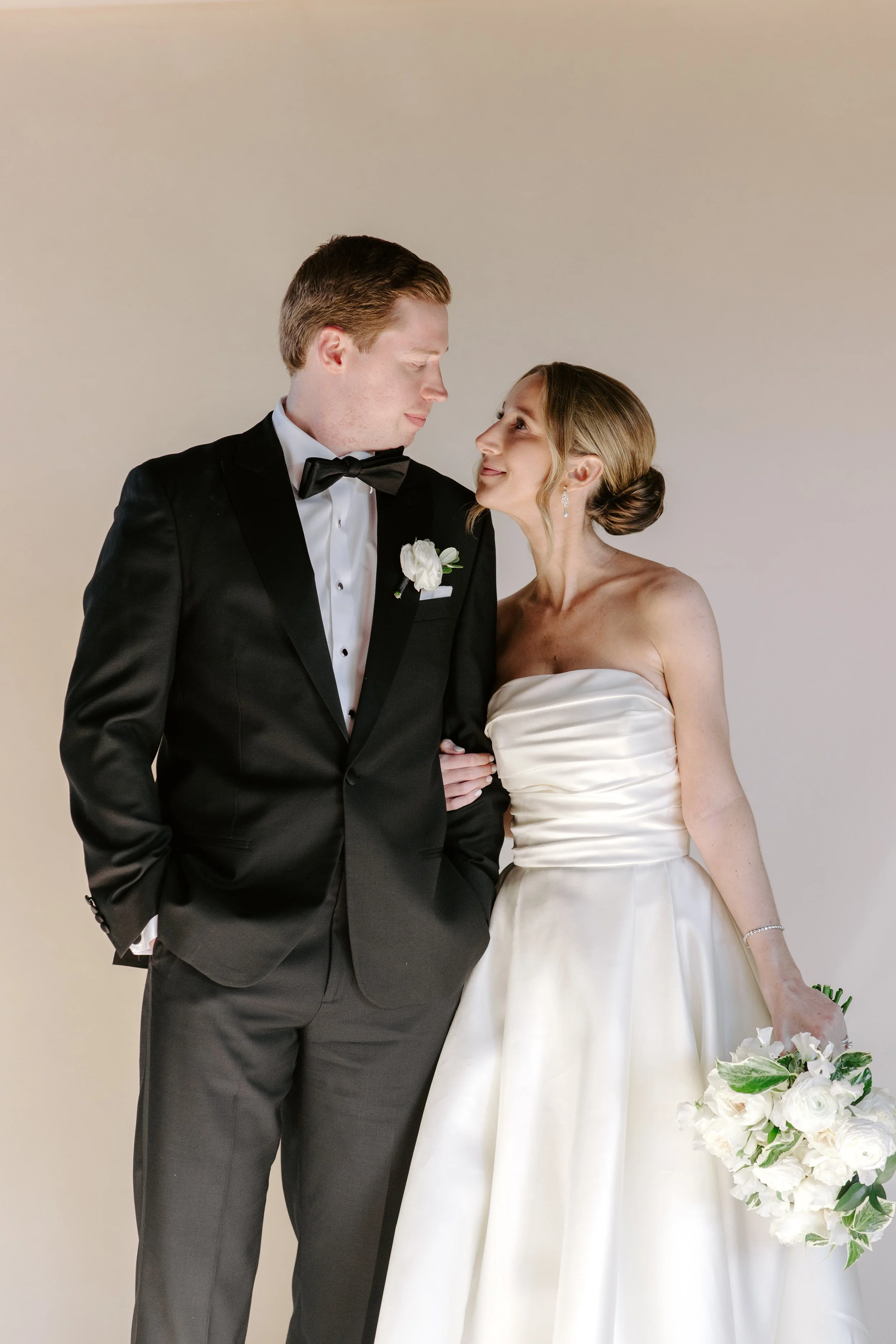A bride and groom standing close together, gazing into each other's eyes, with the bride holding a bouquet of white flowers.