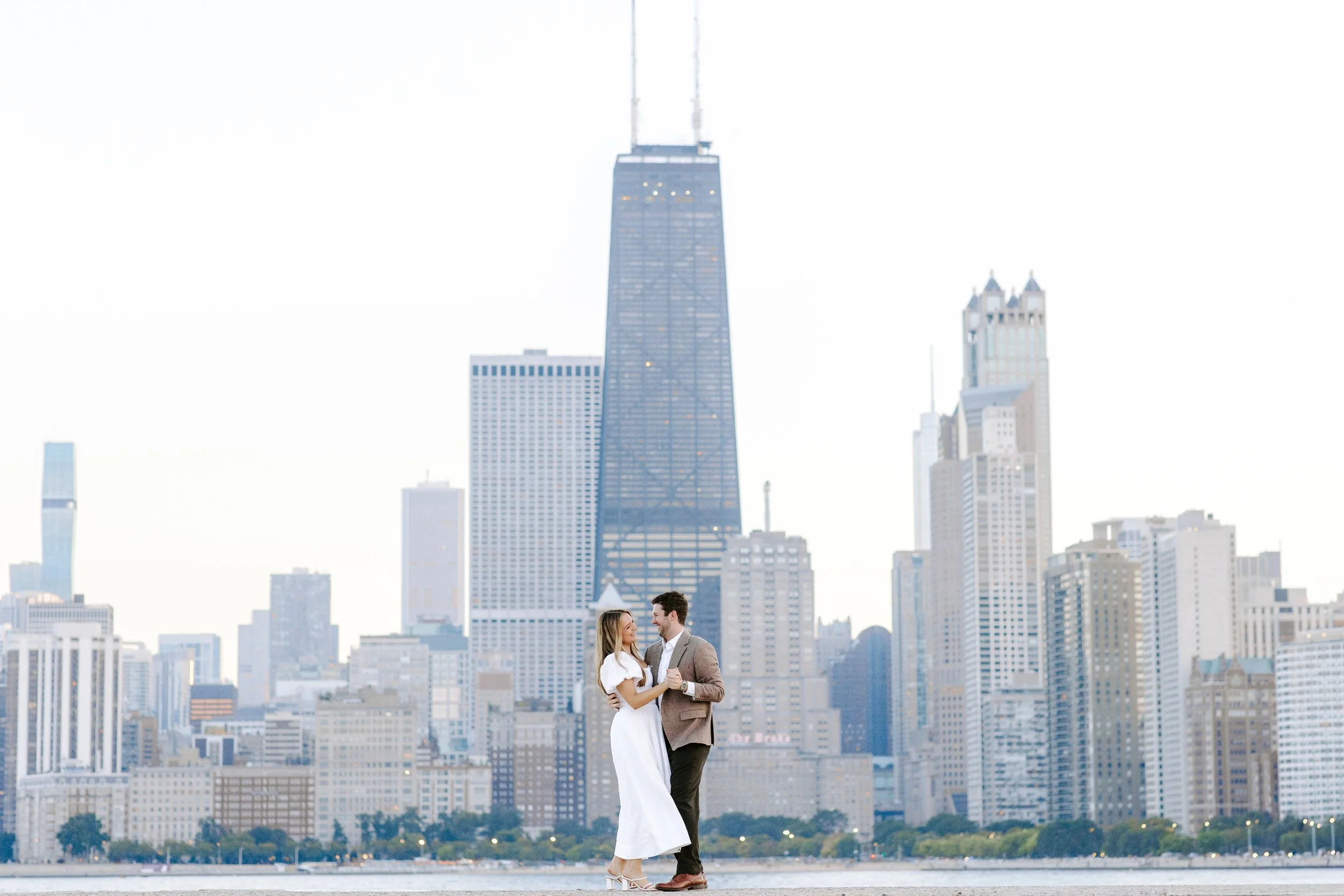 A couple joins hands and looks at each other with the New York City skyline, including the One World Trade Center, in the background.