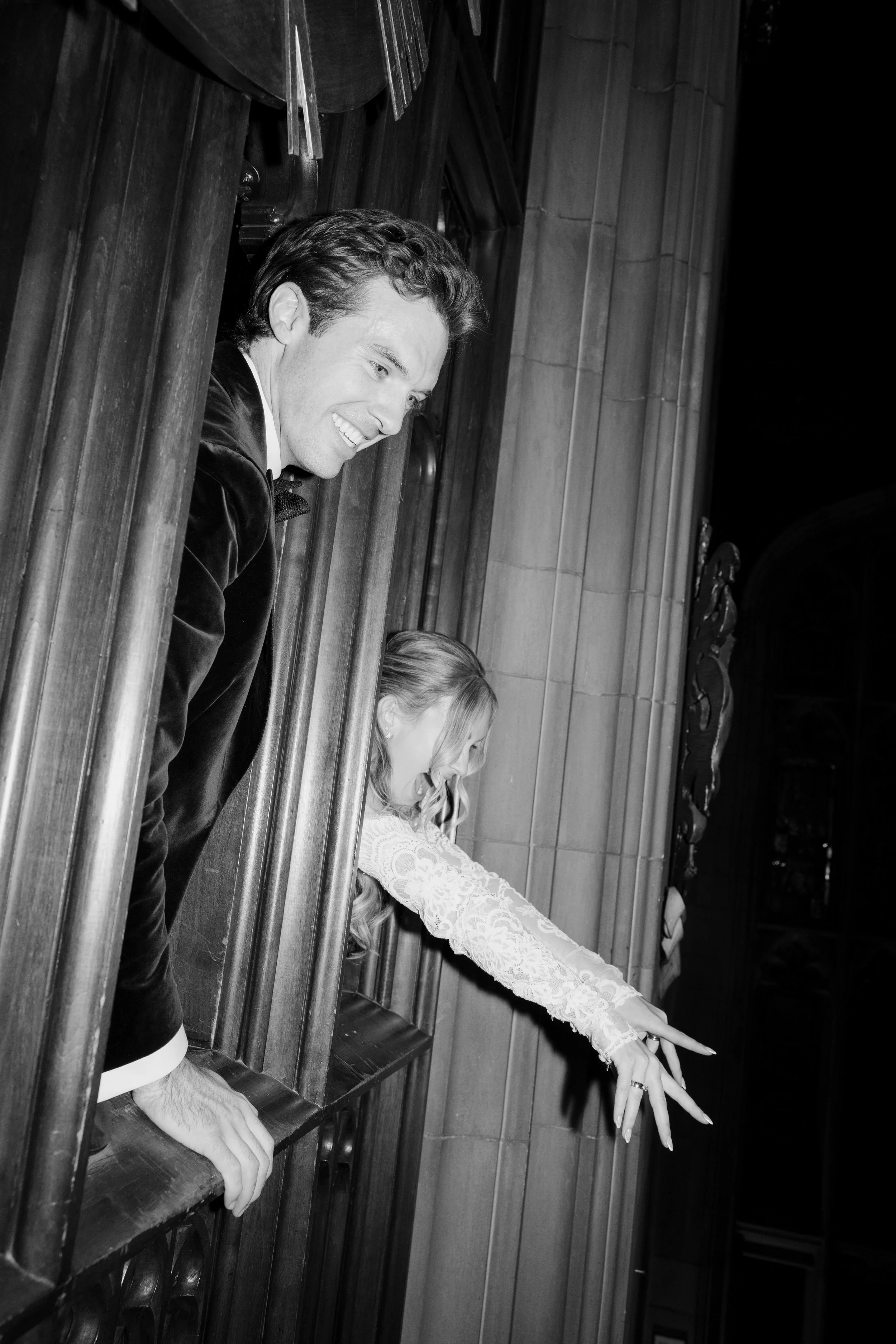 A black and white photo showing a man in a suit and a woman in a lace dress standing at church pews, with their arms extended forward and fingers pointing out.