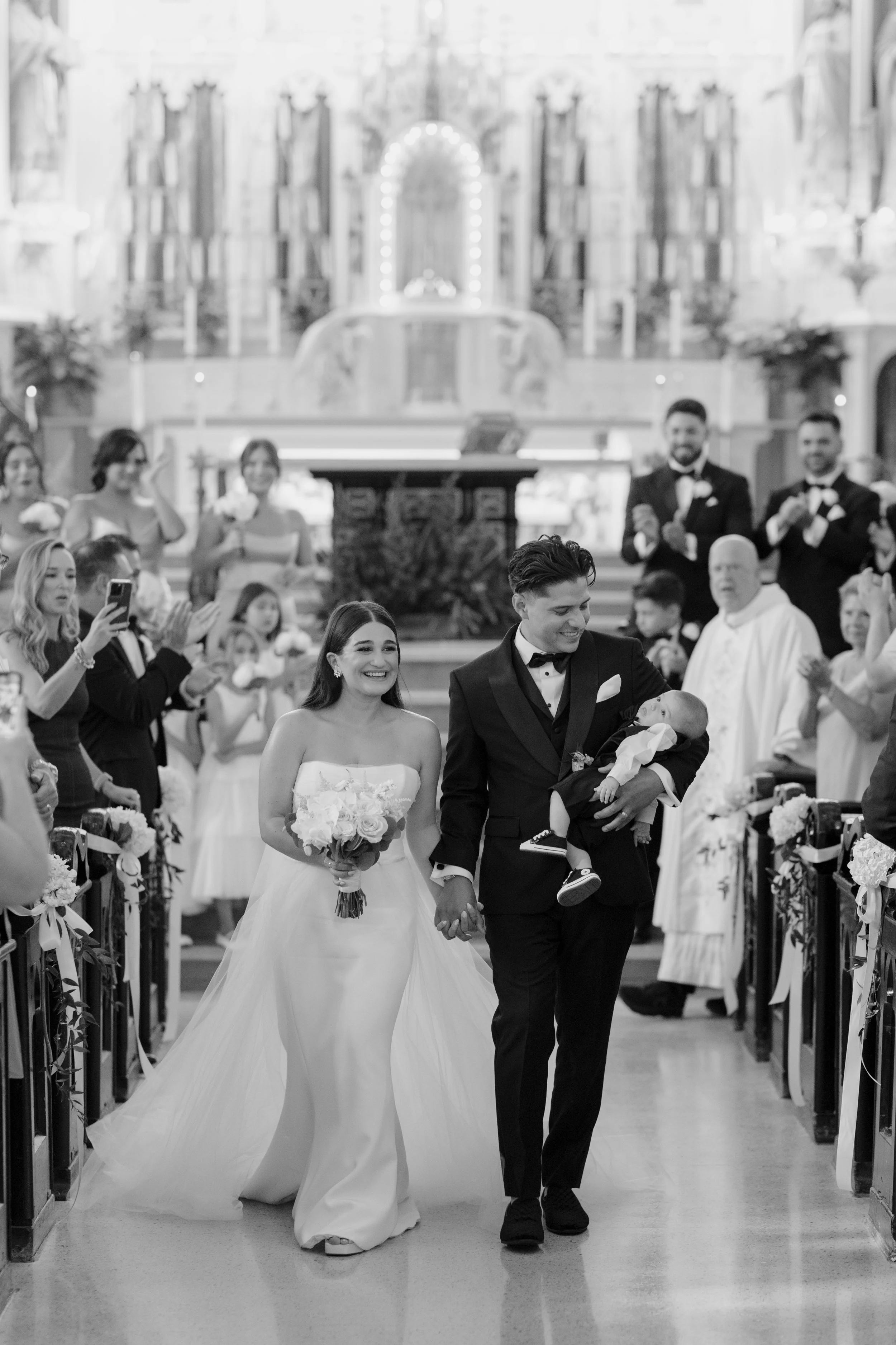 A bride and groom walking down the aisle of a church after their wedding ceremony, holding hands and smiling, surrounded by guests and the church interior.