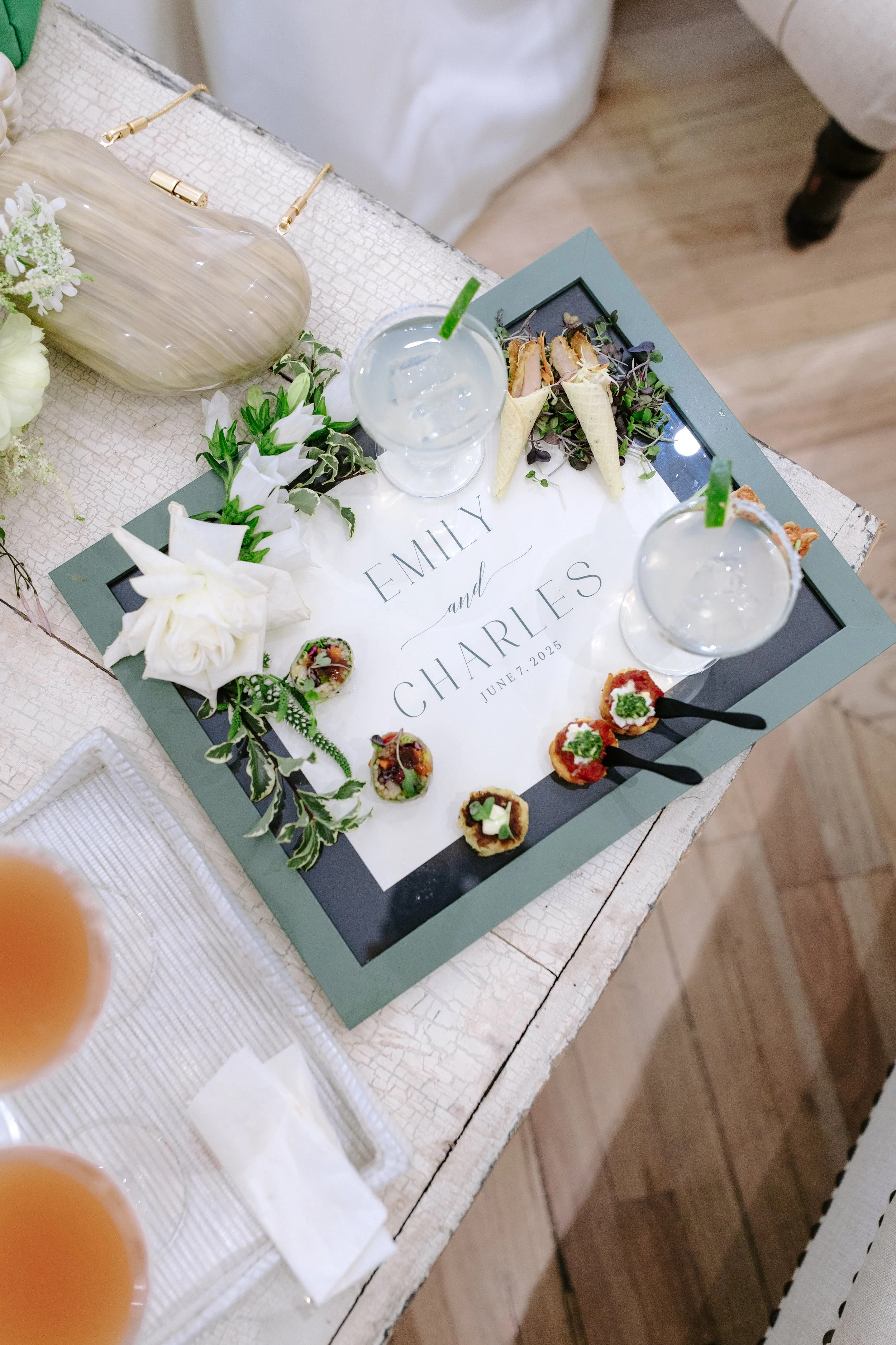 A wedding reception table with floral decorations, drinks, and a personalized sign for Emily and Charles, dated June 7, 2025.