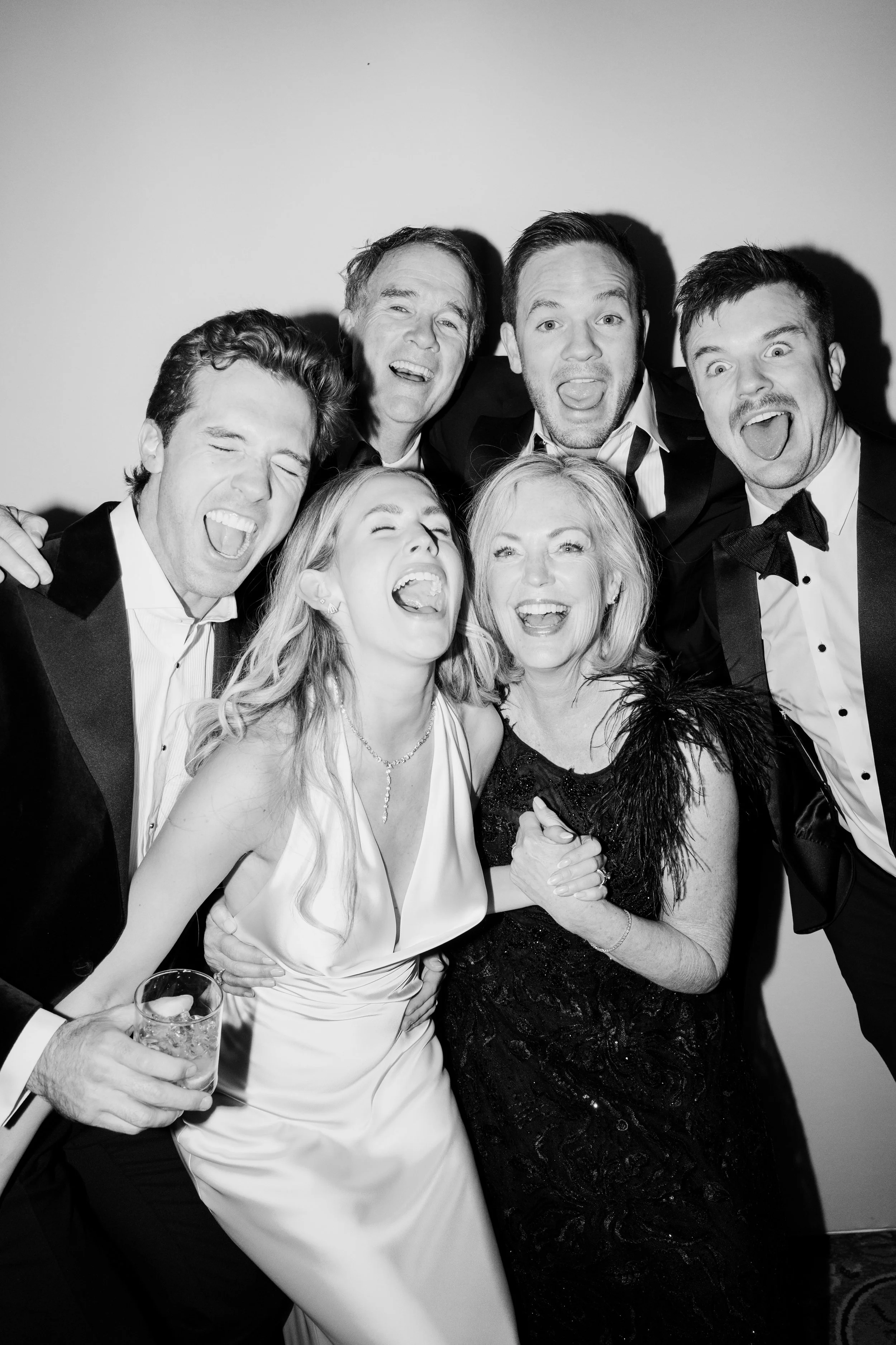 Black and white photo of a group of people dressed in formal attire, celebrating and laughing closely together at a party or event.