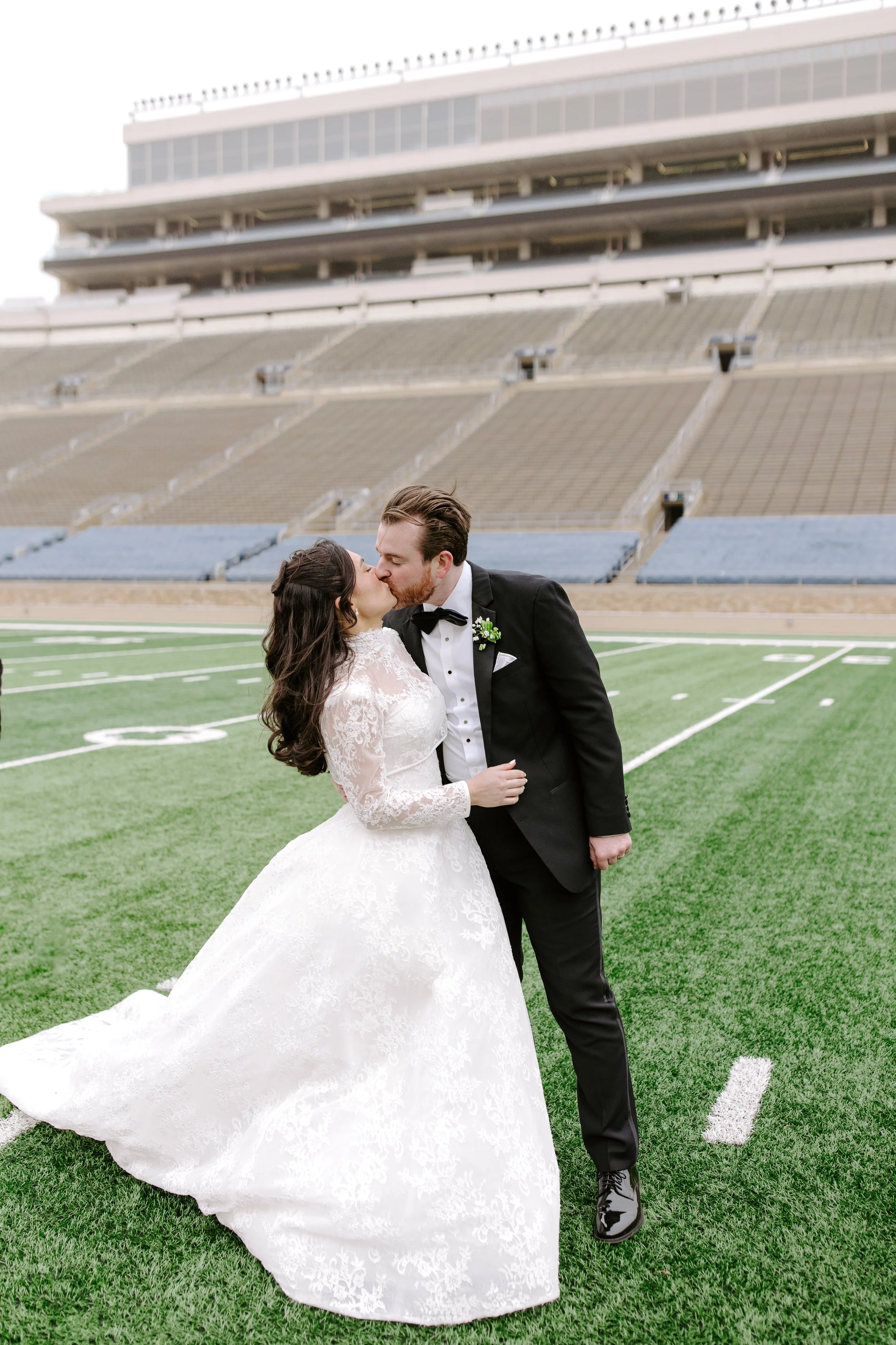 A bride and groom kissing on a football field at a stadium.