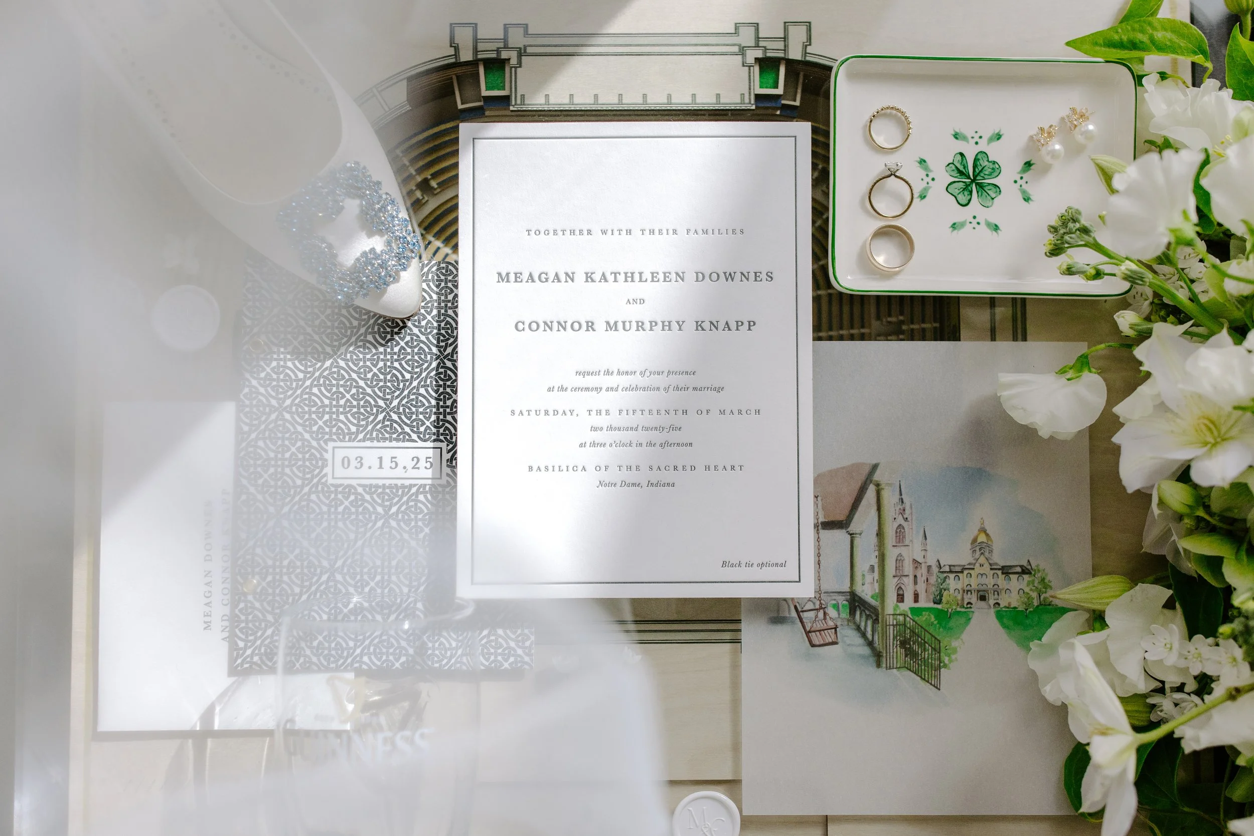 Wedding invitation with white and metallic silver design, wedding date 03.15.25, surrounded by jewelry box with rings, earrings, flower accessories, and white flowers on the right side.