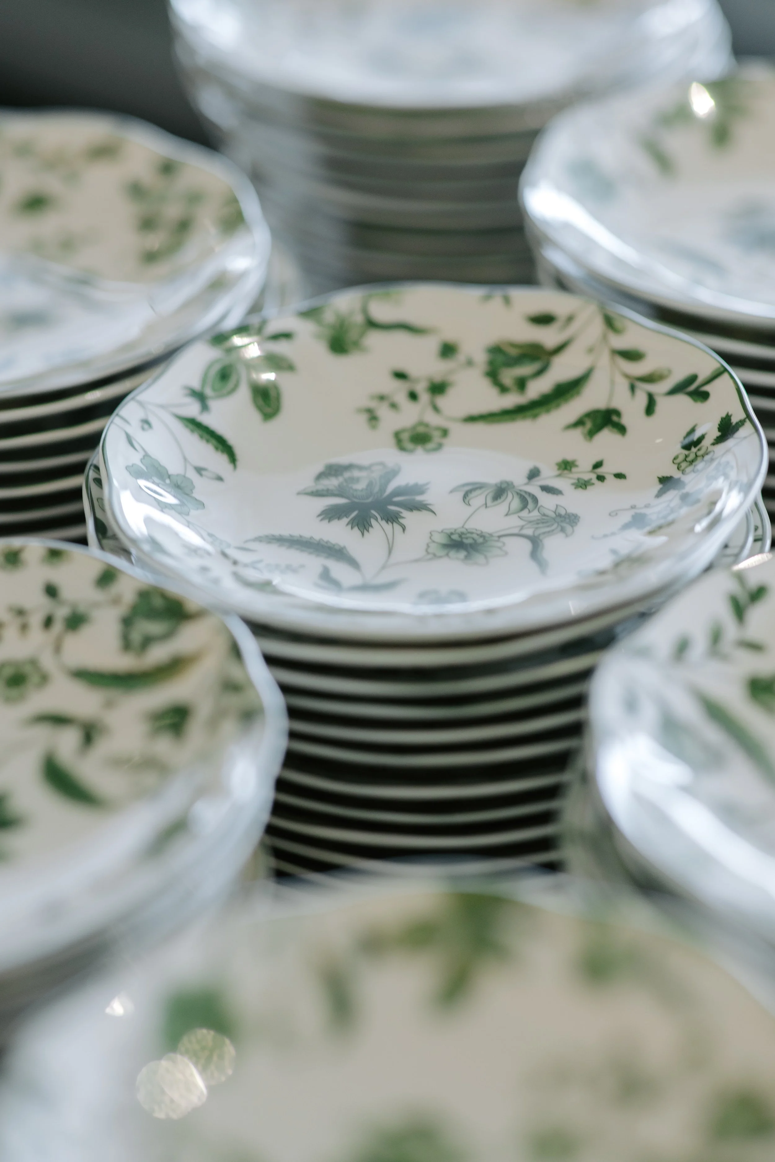 Close-up of a stack of white dishes with green floral patterns.