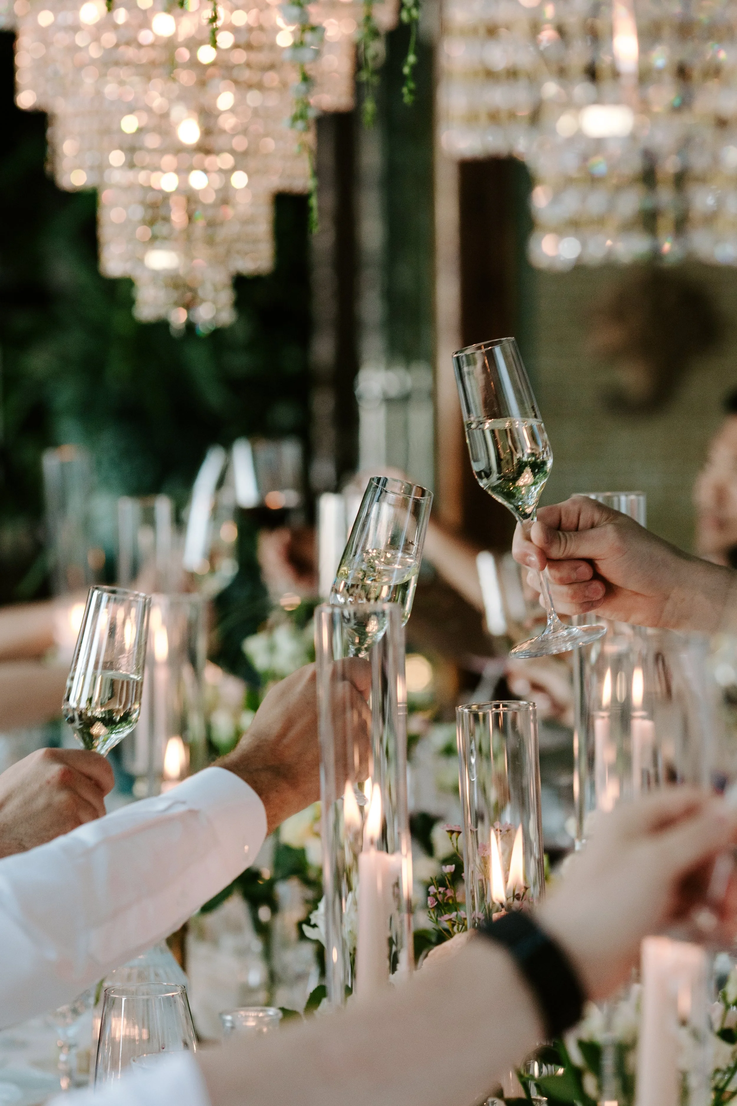 People raising champagne glasses in a toast at an elegant celebration, with a decorated table and warm lighting background.