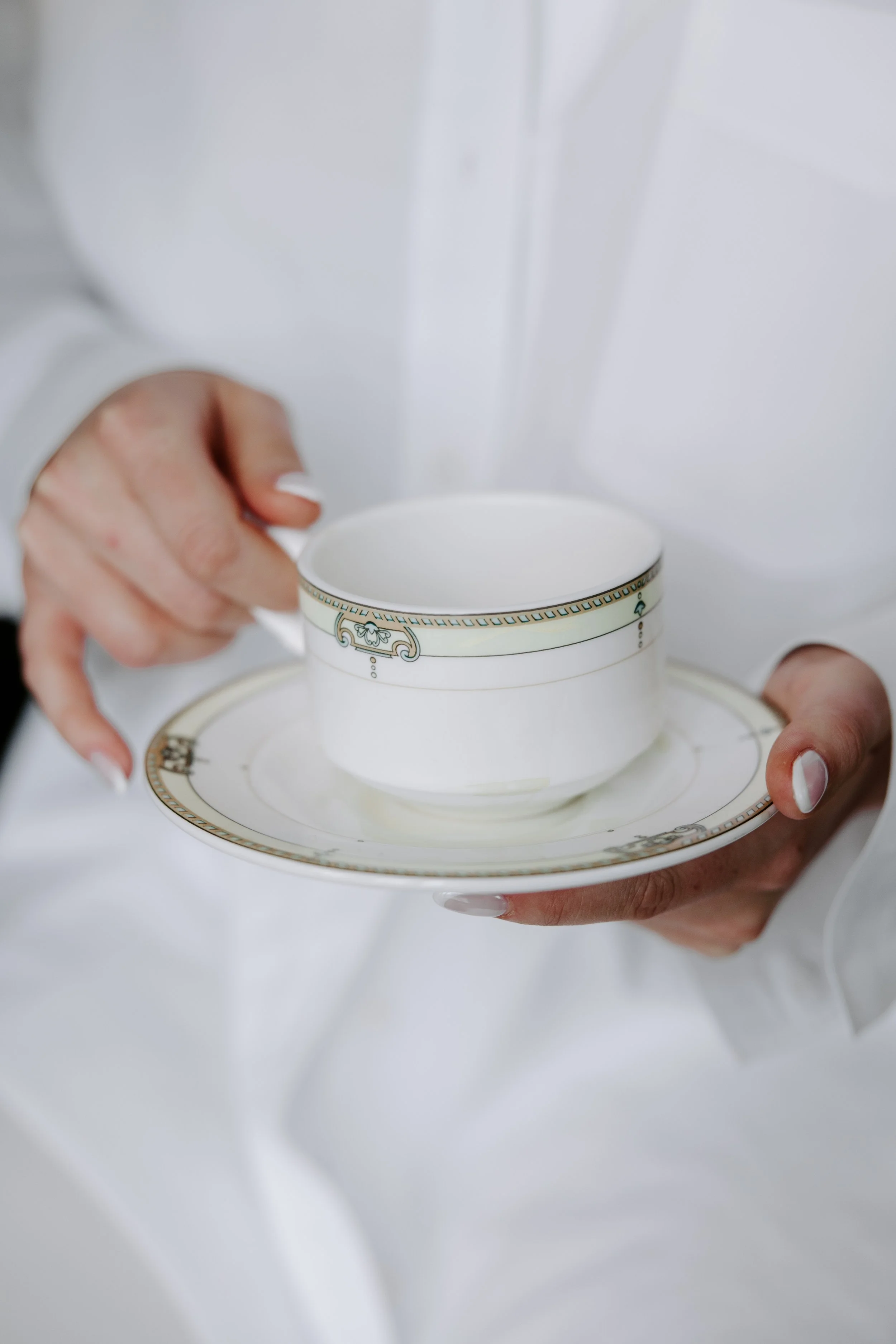 Person holding a decorated teacup and saucer plate against a white background, with a slightly blurred hand.