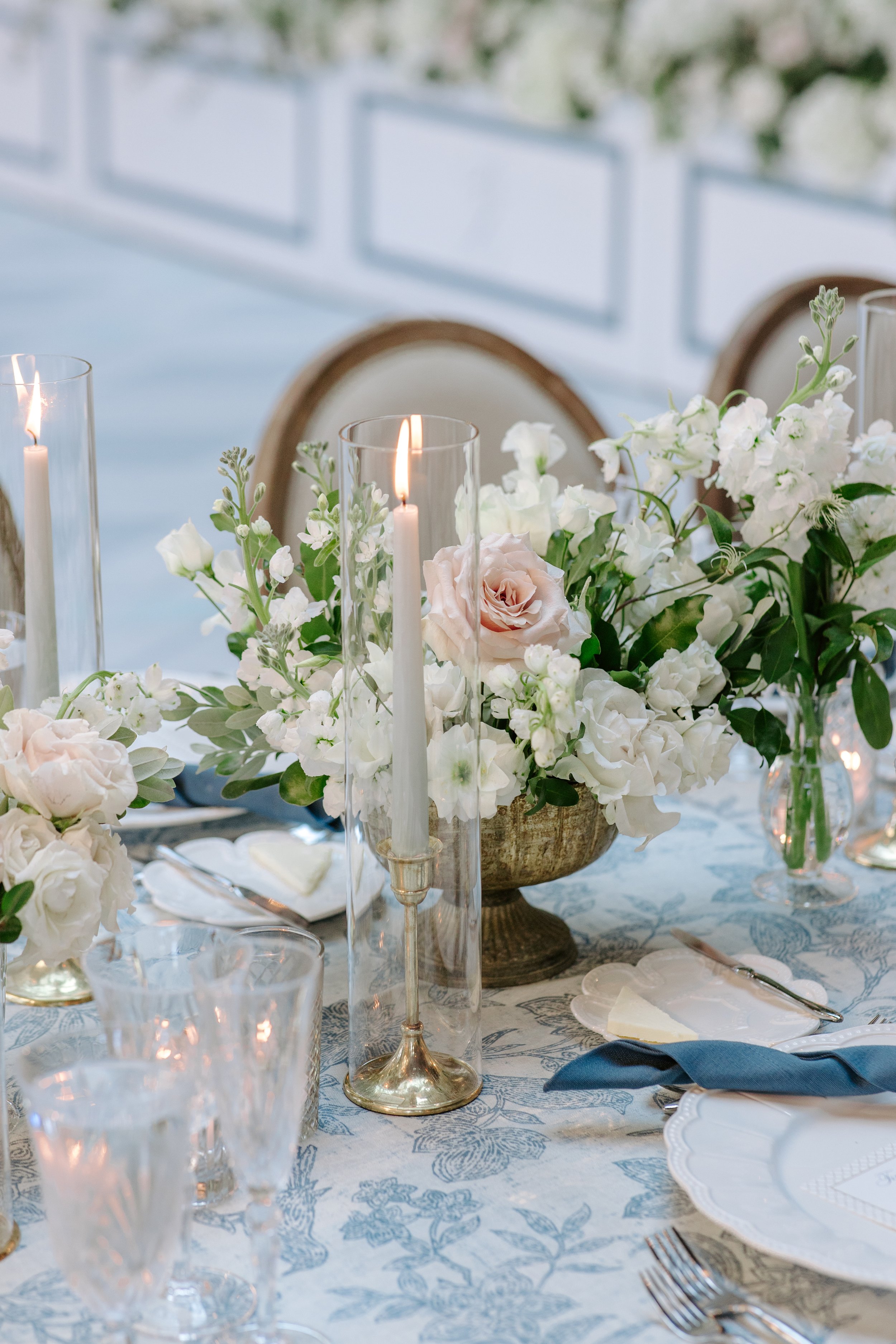 Elegant table setting with floral centerpiece, candles, glassware, and fine china on a patterned tablecloth at a formal event.