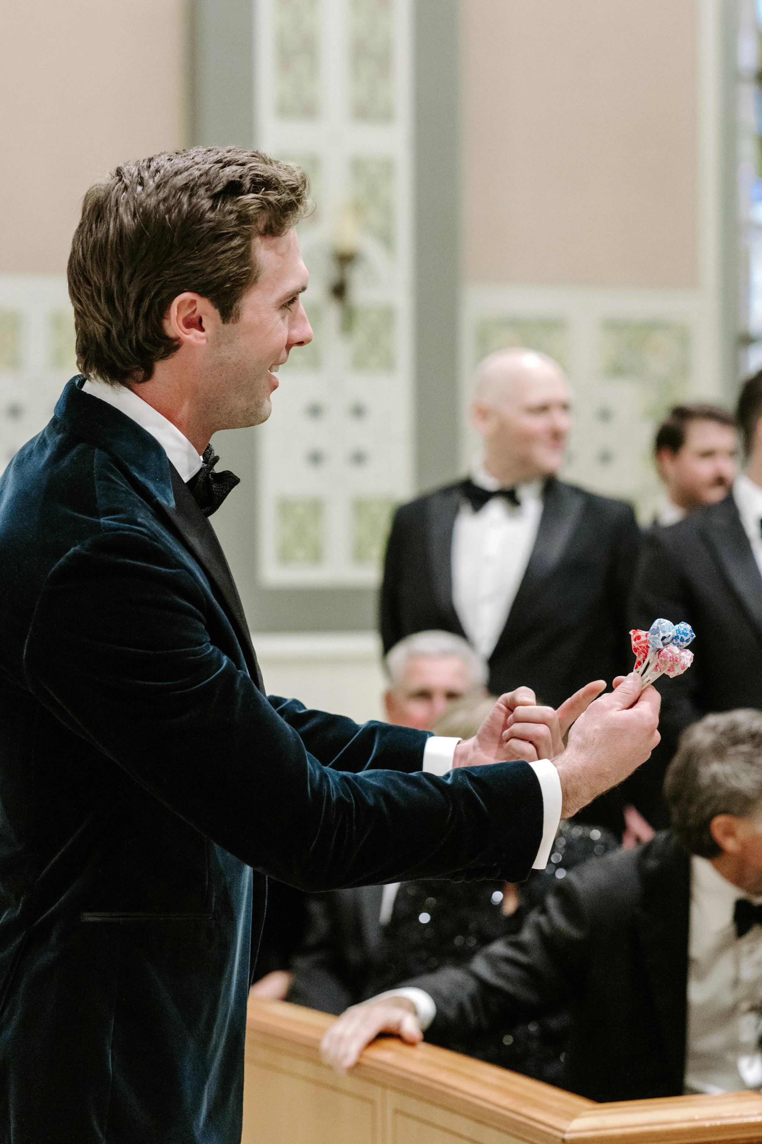 A man in a tuxedo at a formal event, smiling and holding a bouquet of wrapped candies.
