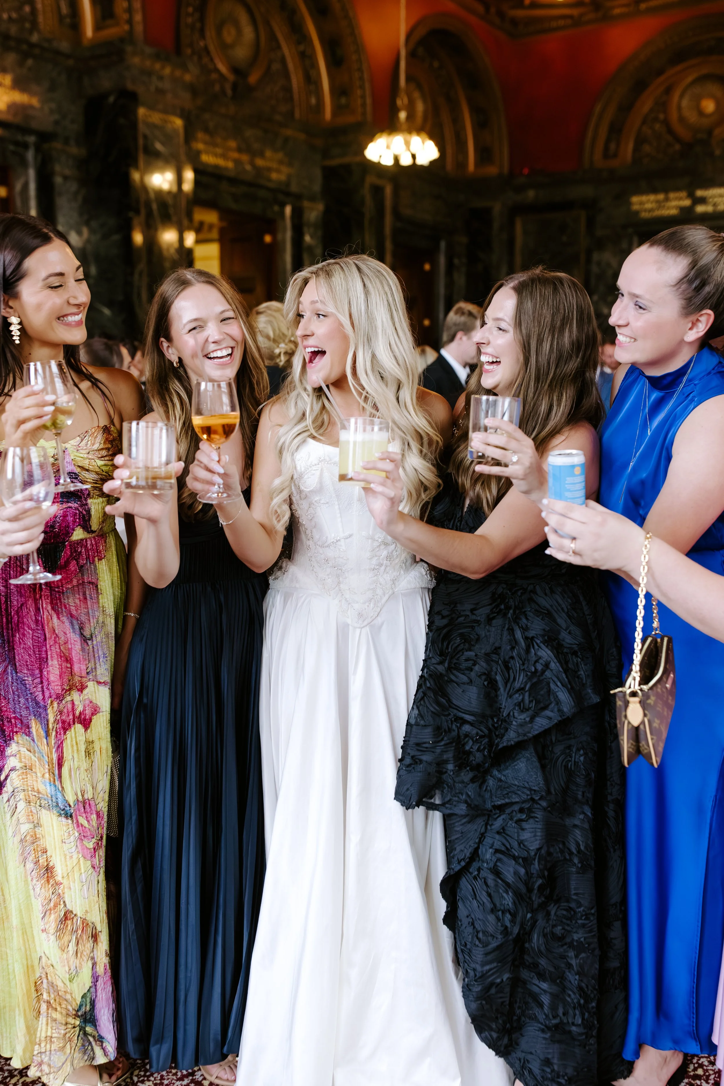 Group of women laughing and holding drinks at an indoor event or celebration.
