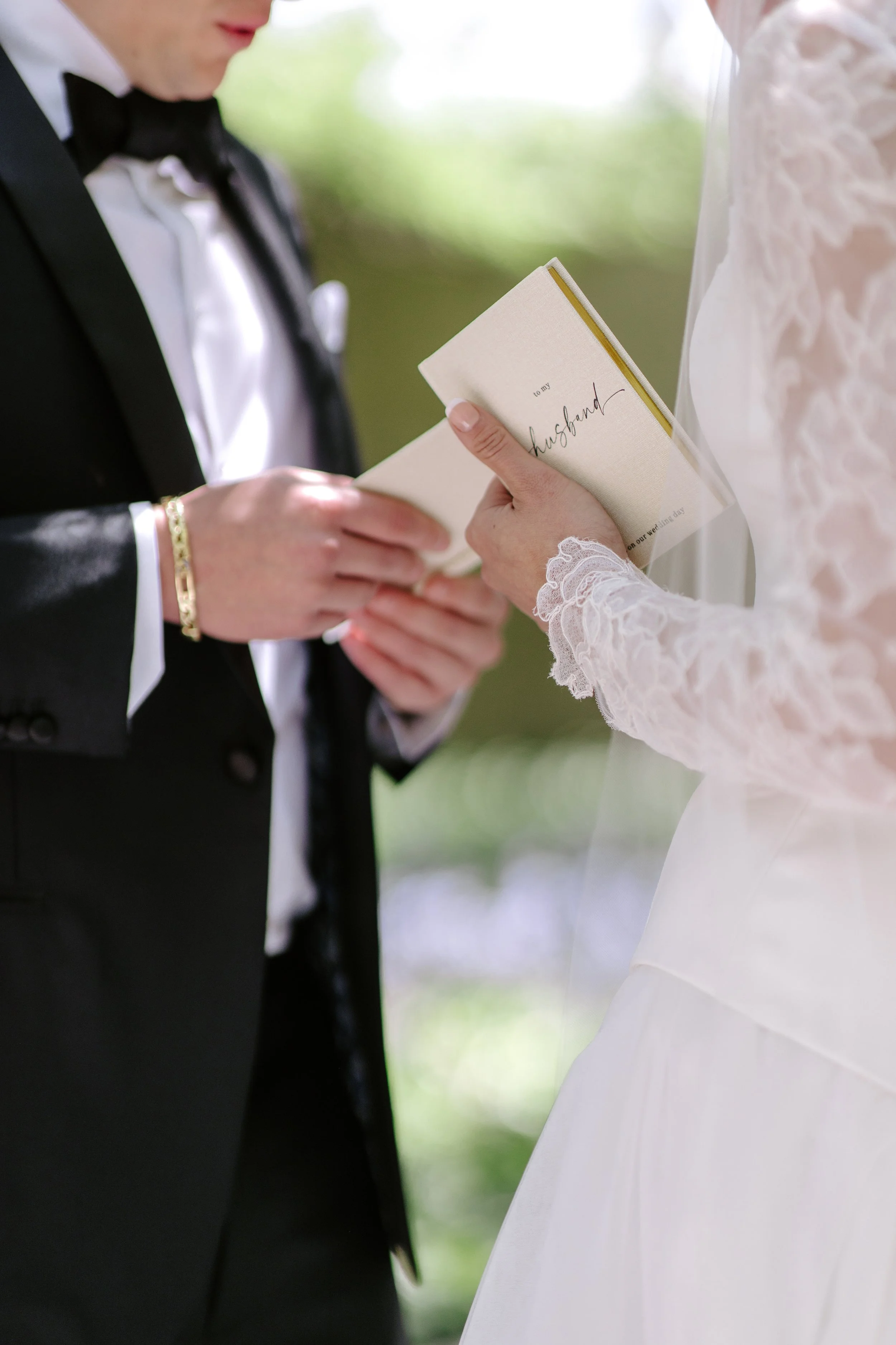 A groom in a black tuxedo holding a wedding vow booklet during a wedding ceremony.