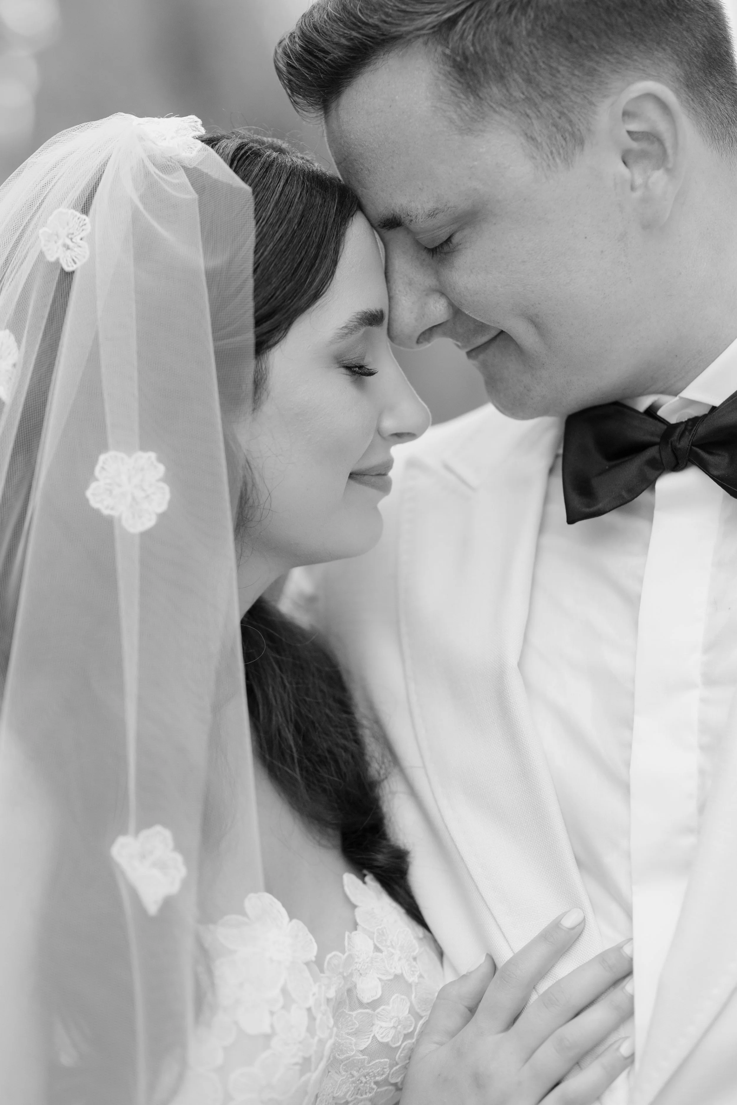 Black and white close-up photo of a bride and groom with foreheads touching, eyes closed, showing that they are in love during their wedding ceremony.
