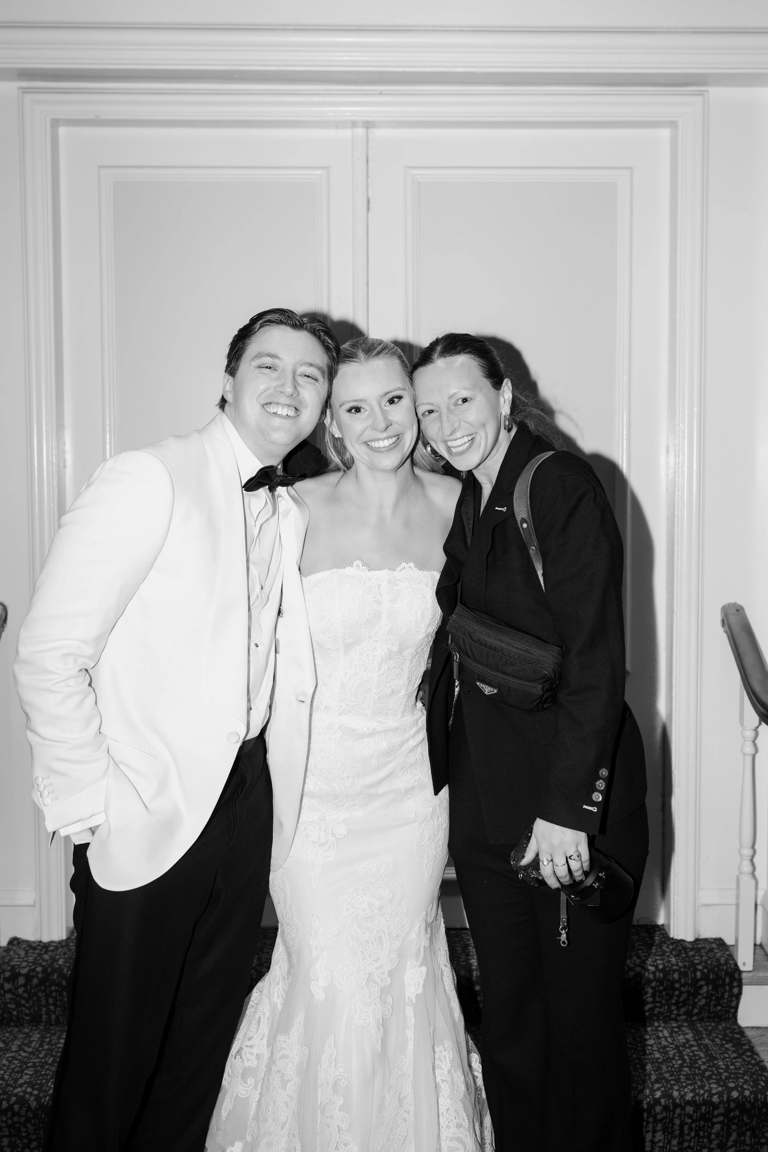 Three people dressed up for a formal event, smiling and standing close together in front of a decorated wall.