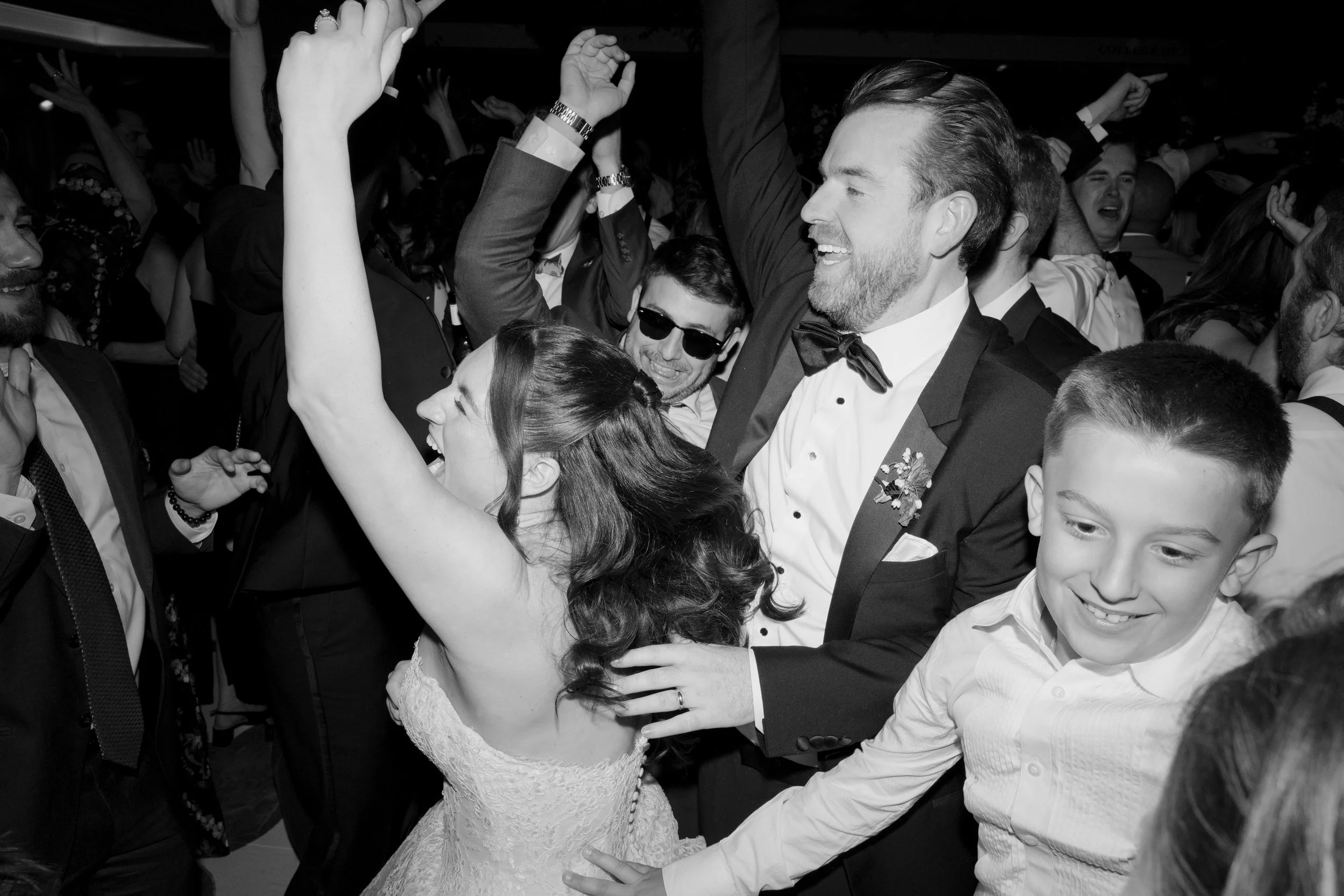 Celebrating a wedding reception with people dancing and smiling, dressed in formal attire, in a festive environment.