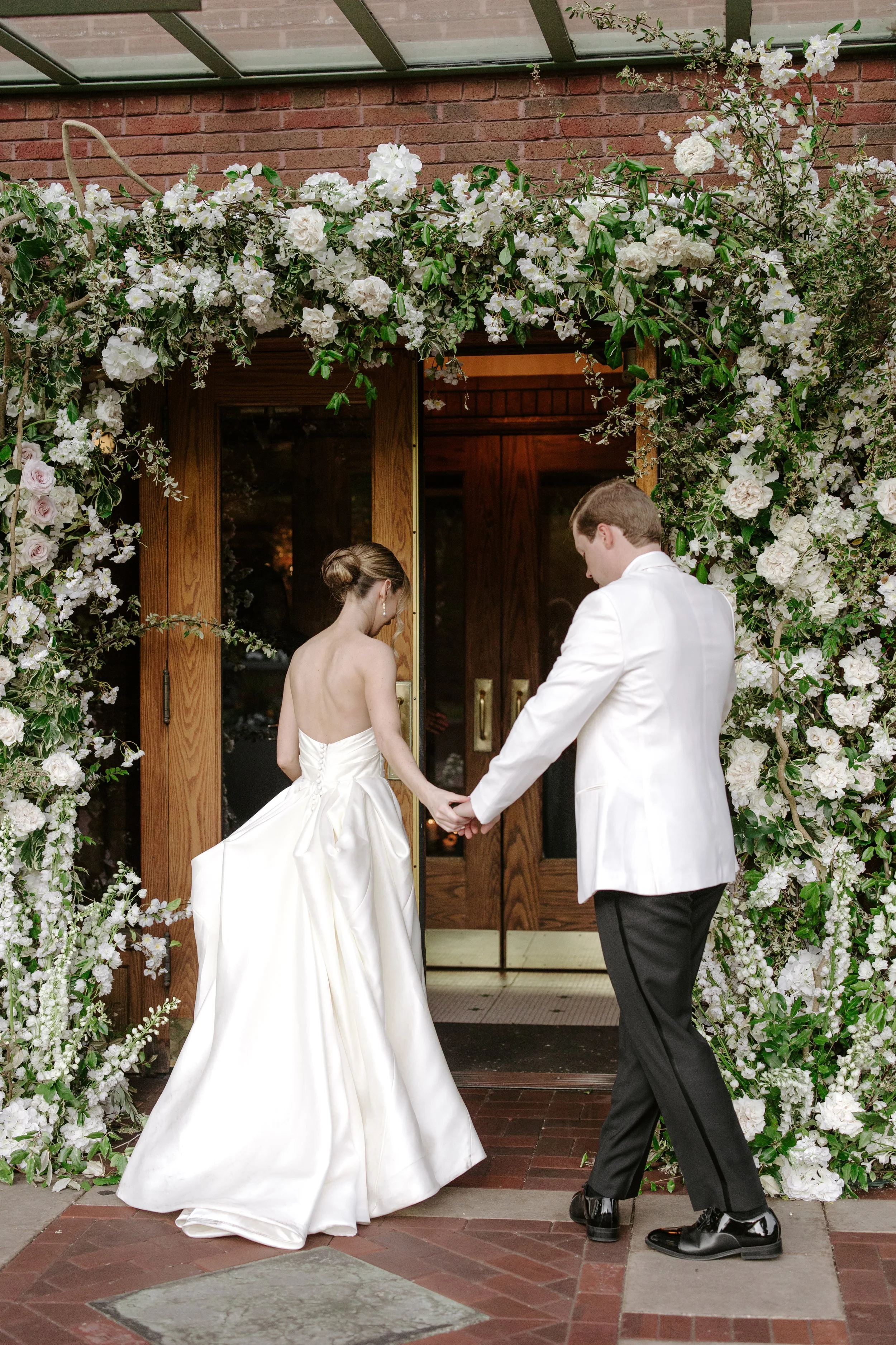A bride and groom holding hands beneath a floral arch during their wedding ceremony.