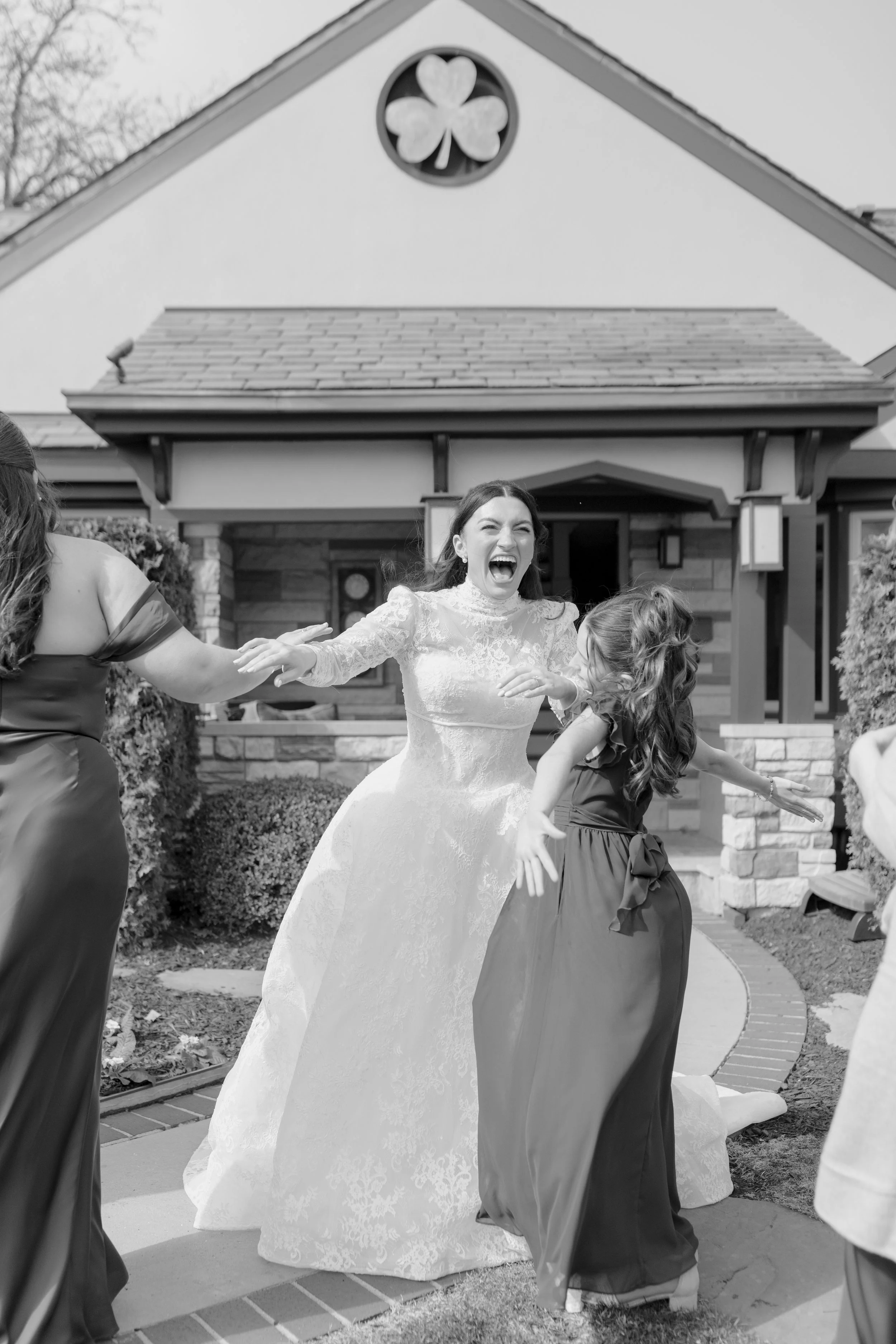 A bride in a wedding gown happily dancing outside a house with children and adults during a celebration.