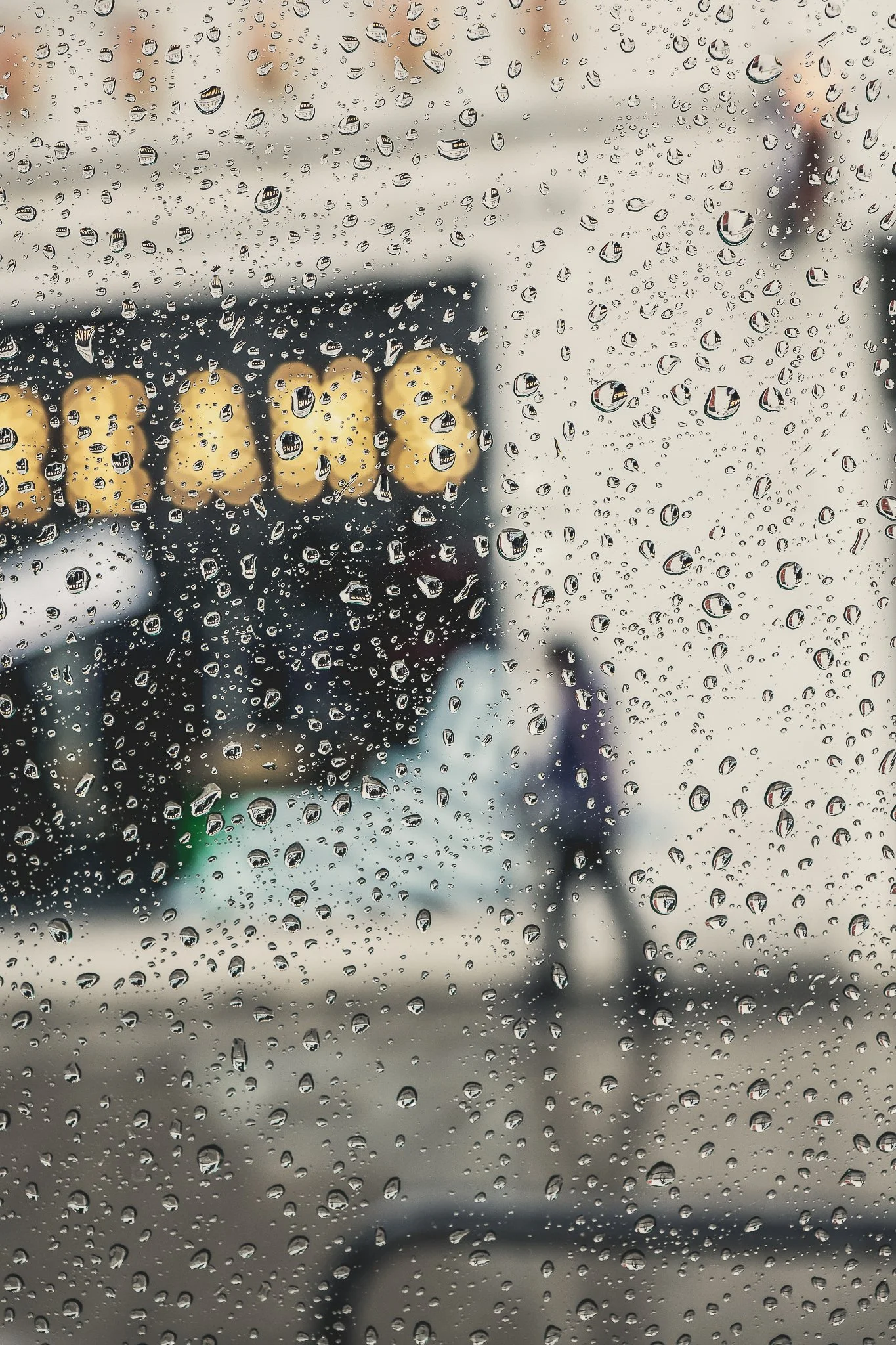 View of traffic lights and blurry city's skyline through a rain-covered window.