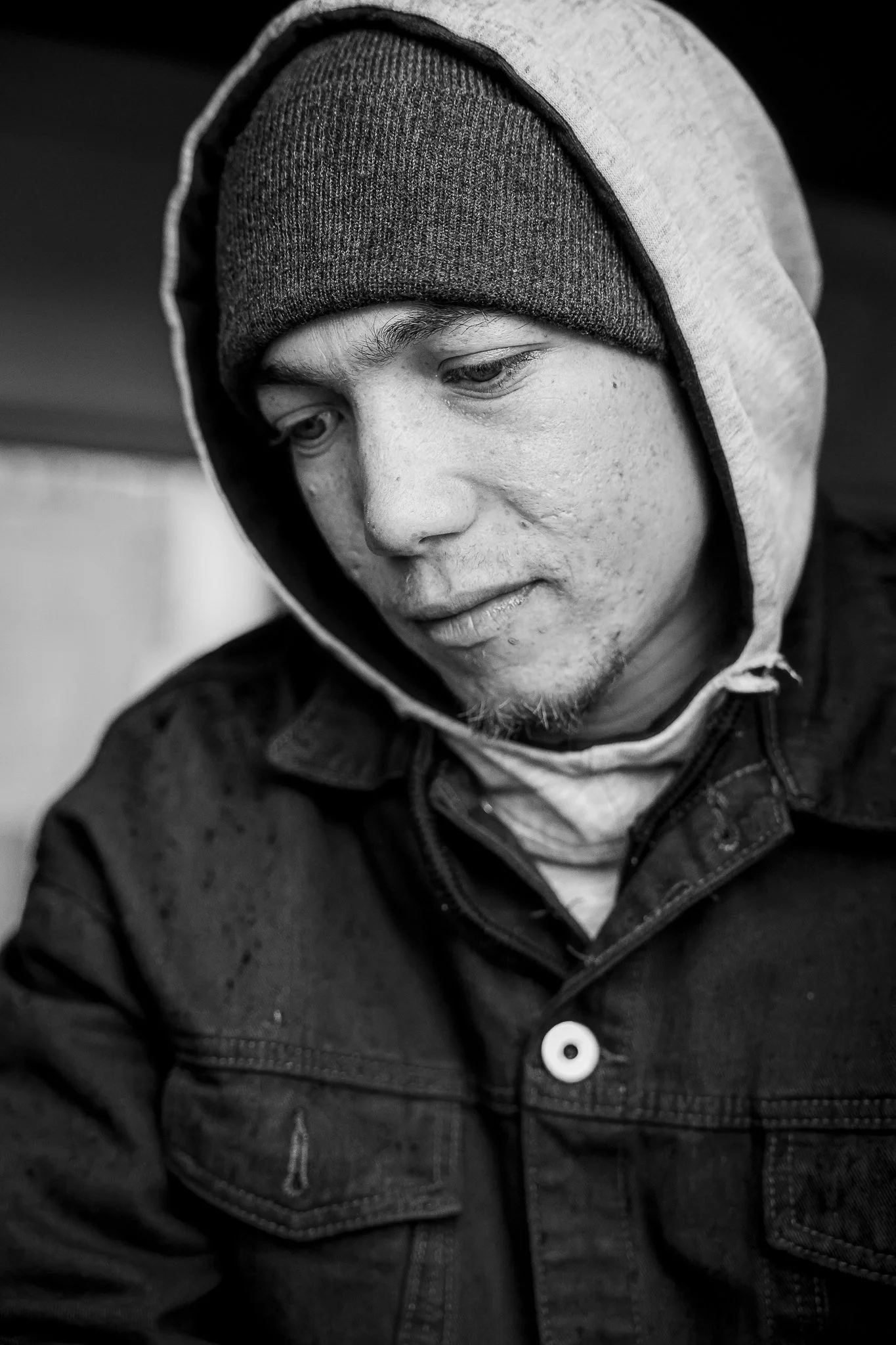 Close-up black and white photo of a young man wearing a hoodie and a beanie, looking down with a contemplative expression.