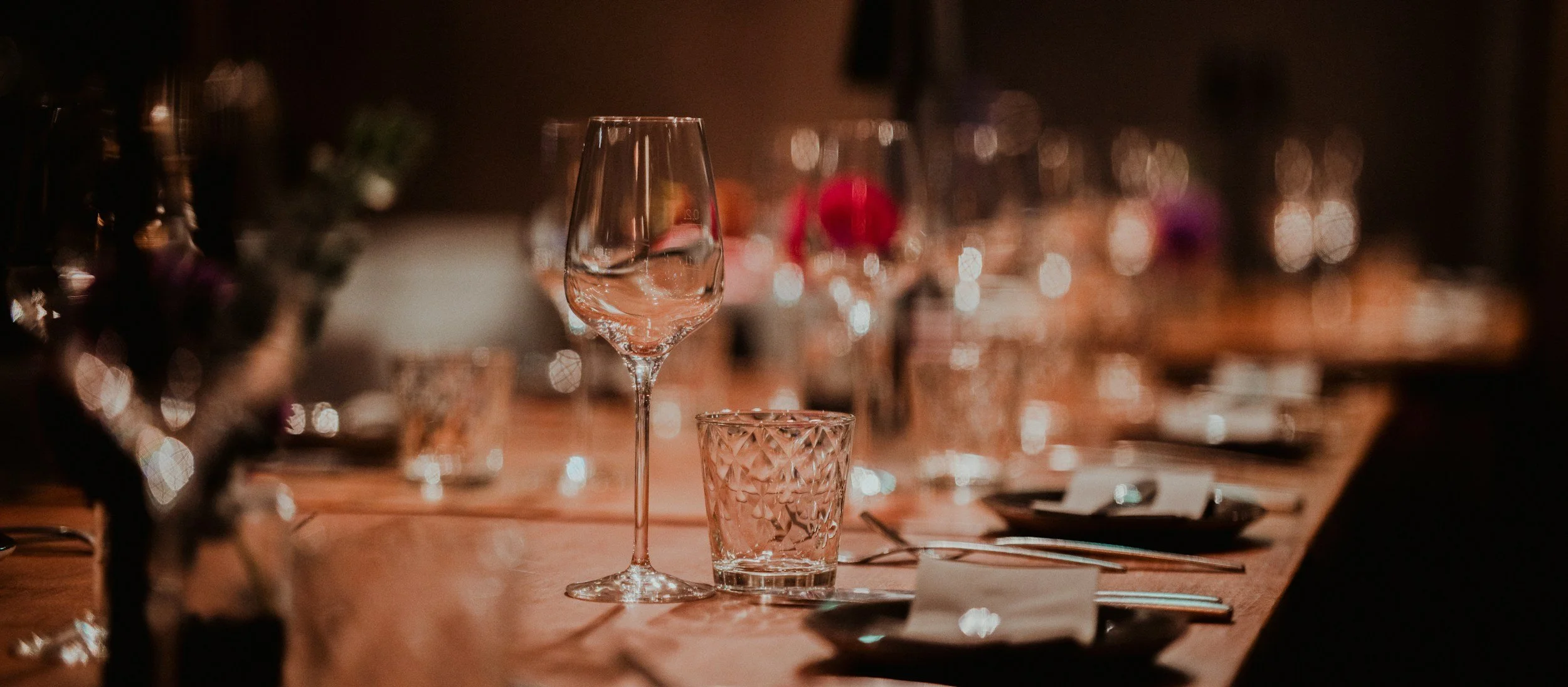 Elegant dining table with wine glasses, water glasses, and floral centerpieces in a dimly lit setting.
